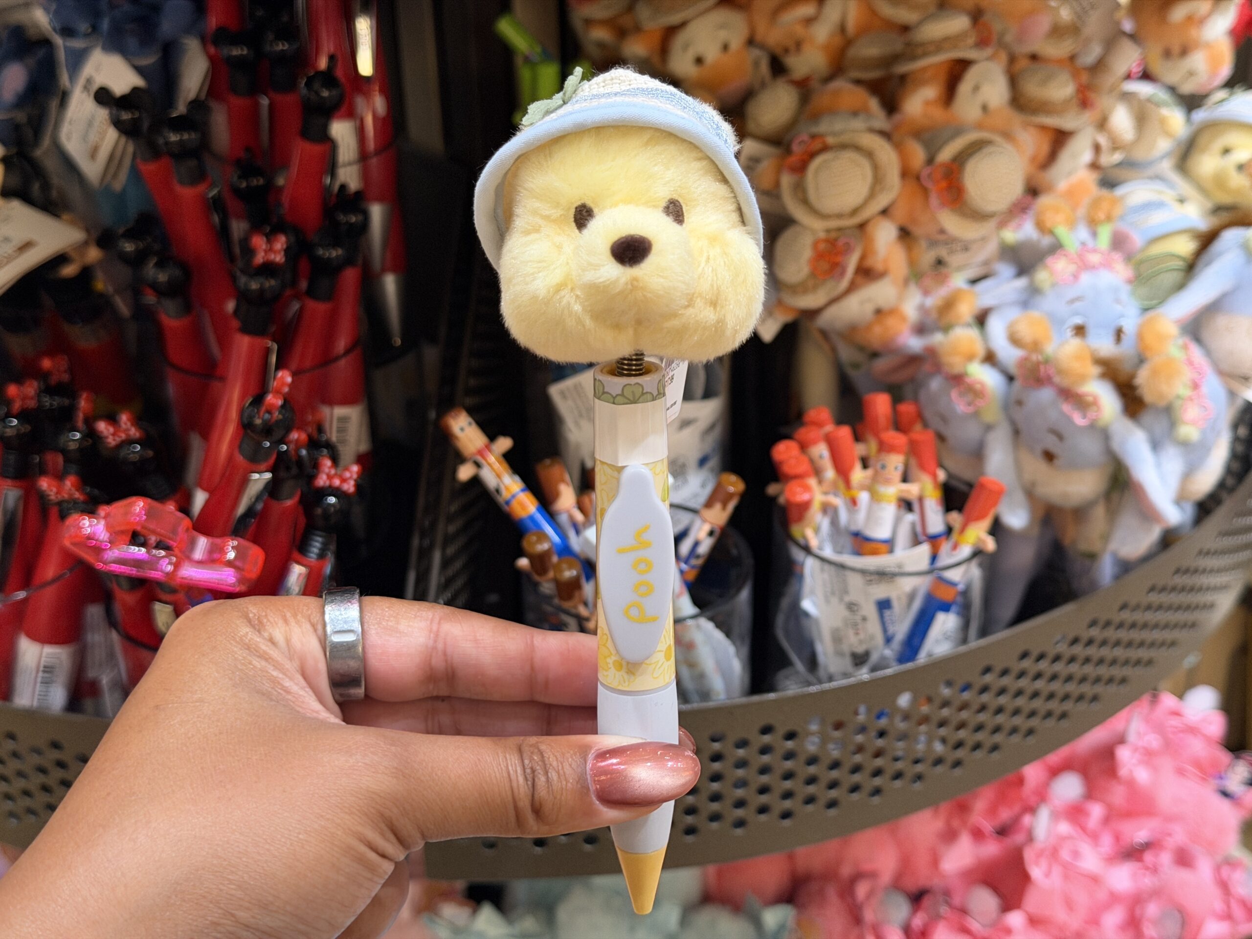The Winnie the Pooh pen has a plush Pooh head wearing a light blue and white rain hat. His face is embroidered with dark eyes and his beady nose.