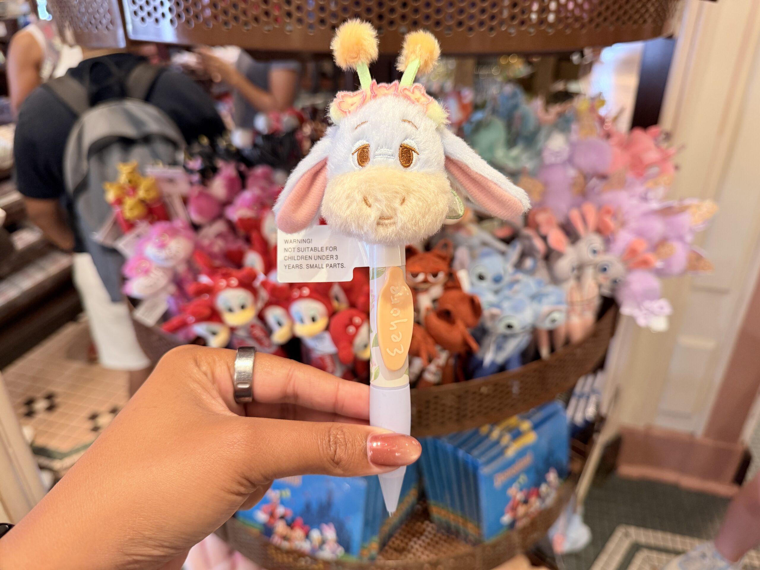 The Eeyore pen features a soft plush head of the gloomy donkey from Winnie the Pooh. Eeyore has pastel pink inner ears, a cream-colored muzzle, and fuzzy yellow antennae with green translucent wings.