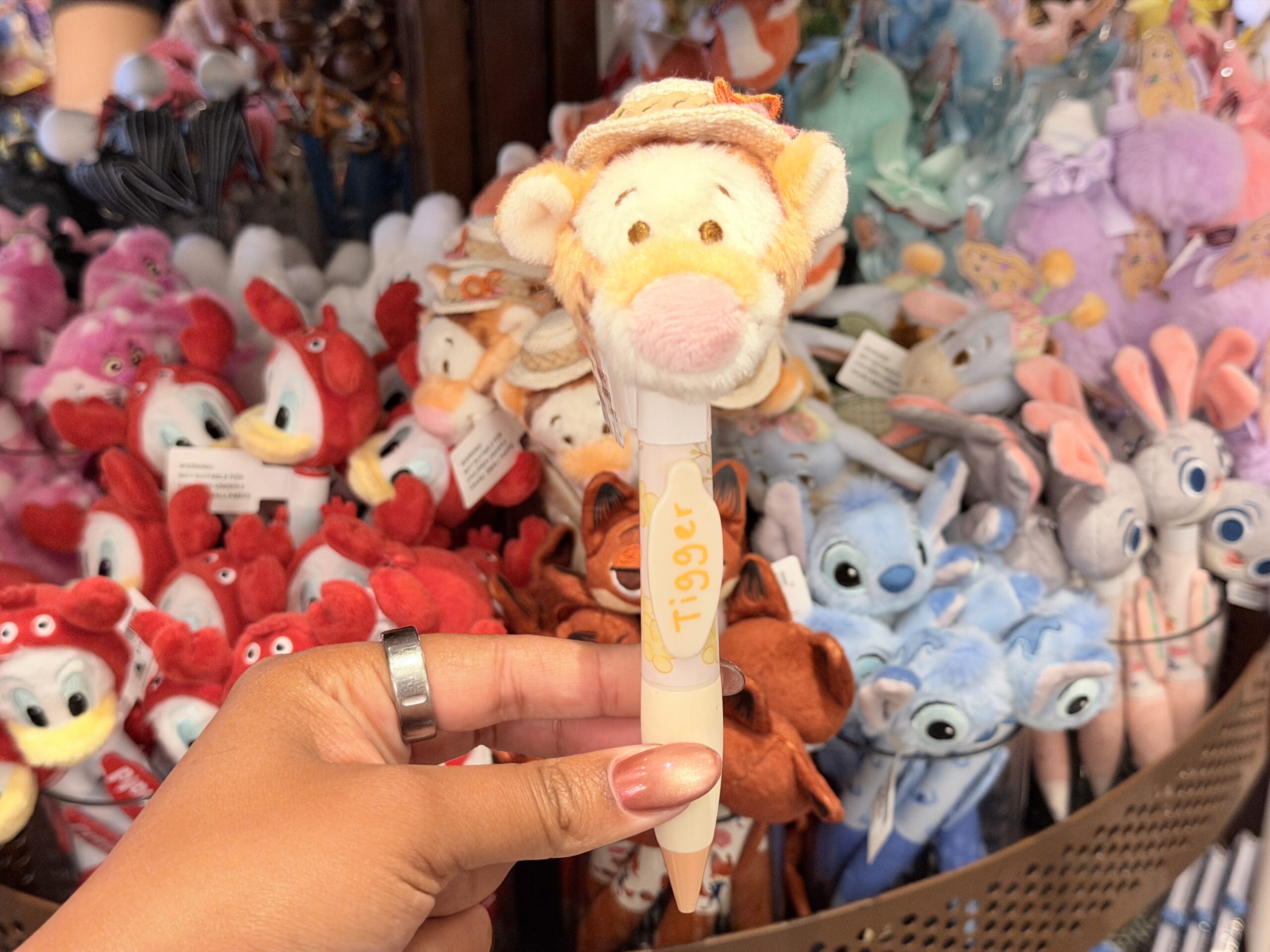 The Tigger pen has a plush Tigger head wearing a small straw hat with orange floral accents. His face features his usual pink nose, embroidered eyes, and orange coloring.