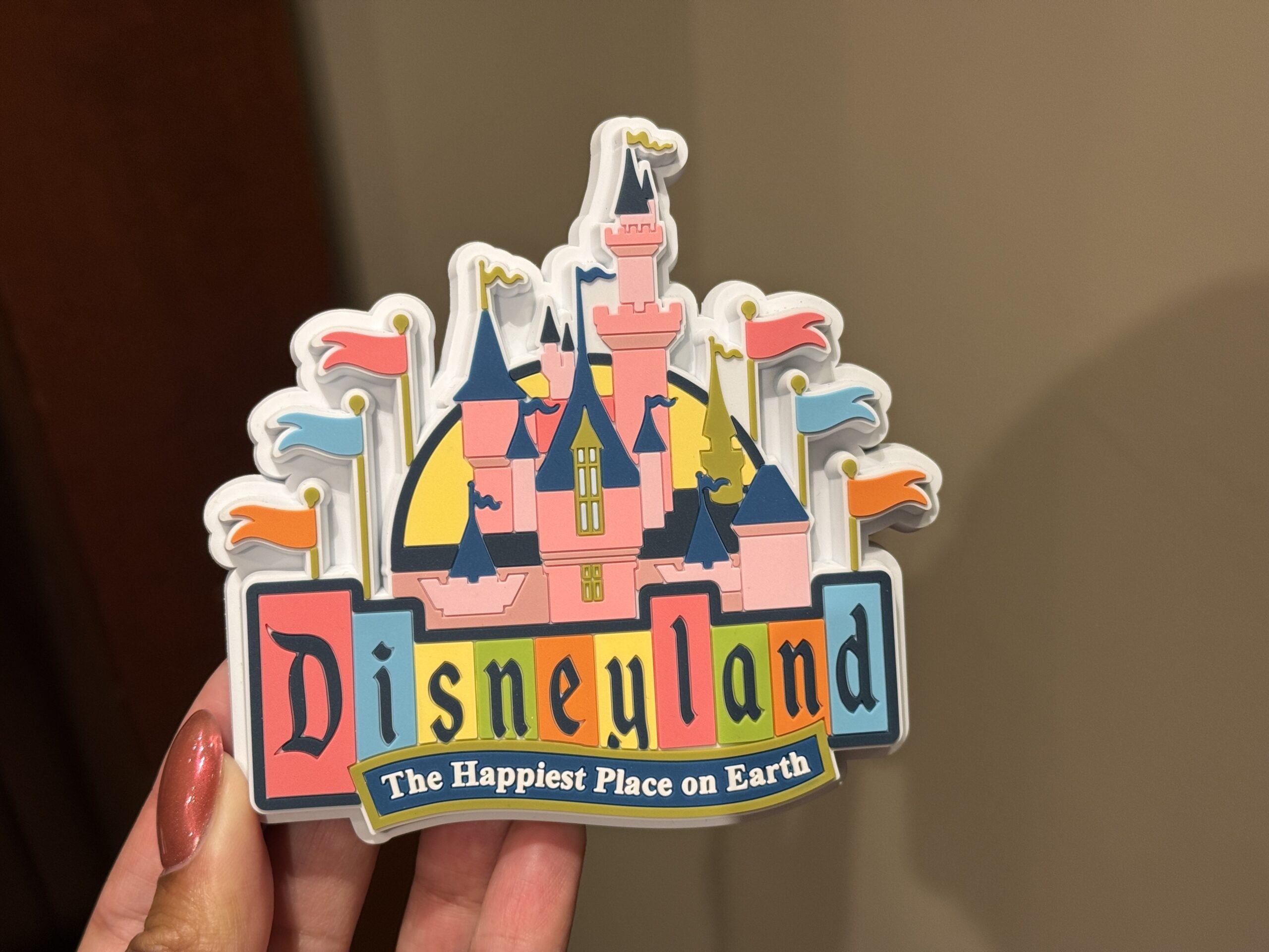 The Disneyland magnet has Sleeping Beauty Castle surrounded by flags and the Disneyland marquee at the bottom, including "The Happiest Place on Earth" text.