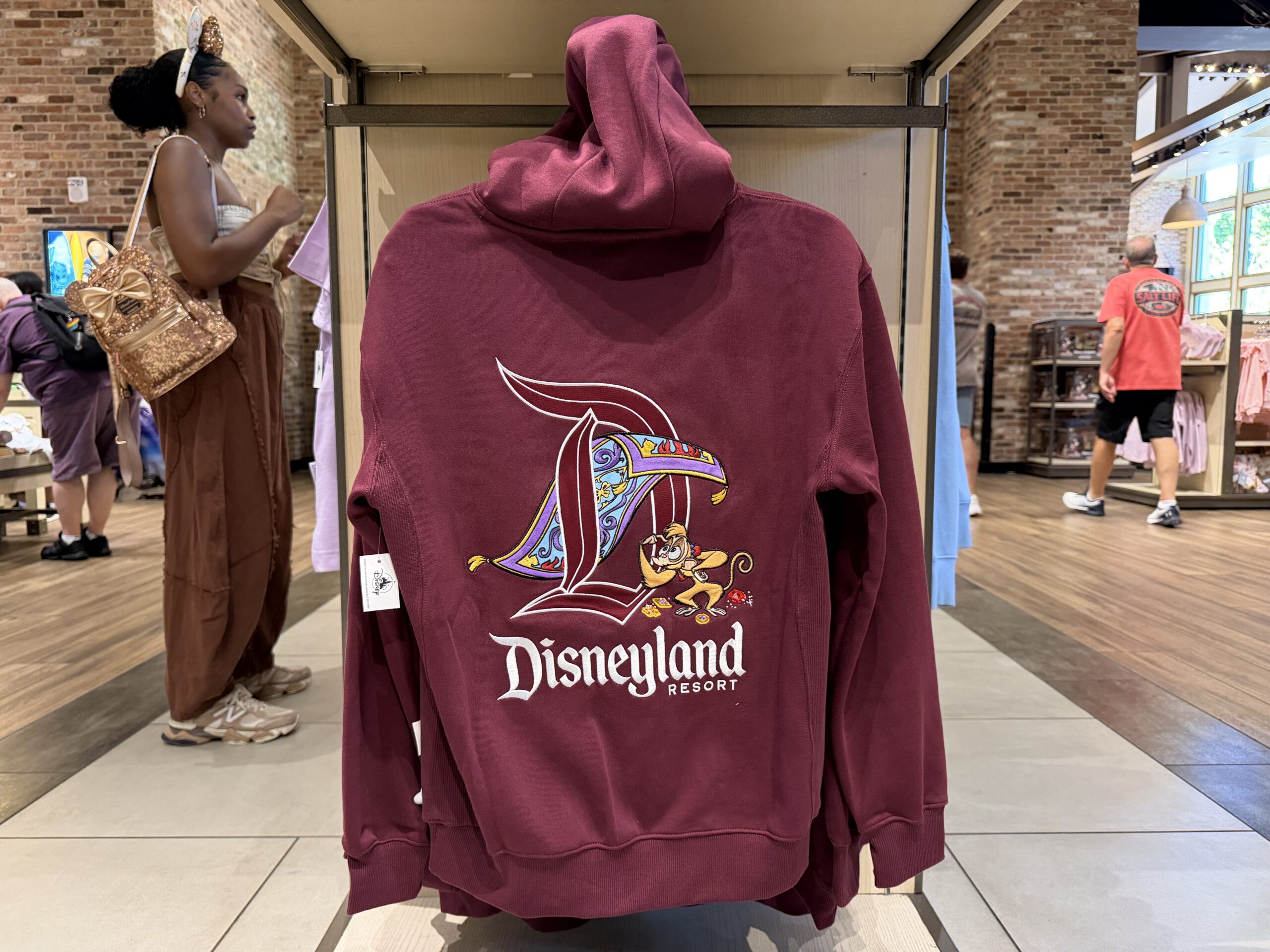 The hoodie is a rusty red. It has a drawstring hood and kangaroo front pocket. Embroidered on the left chest is Genie's lamp and "Disneyland."