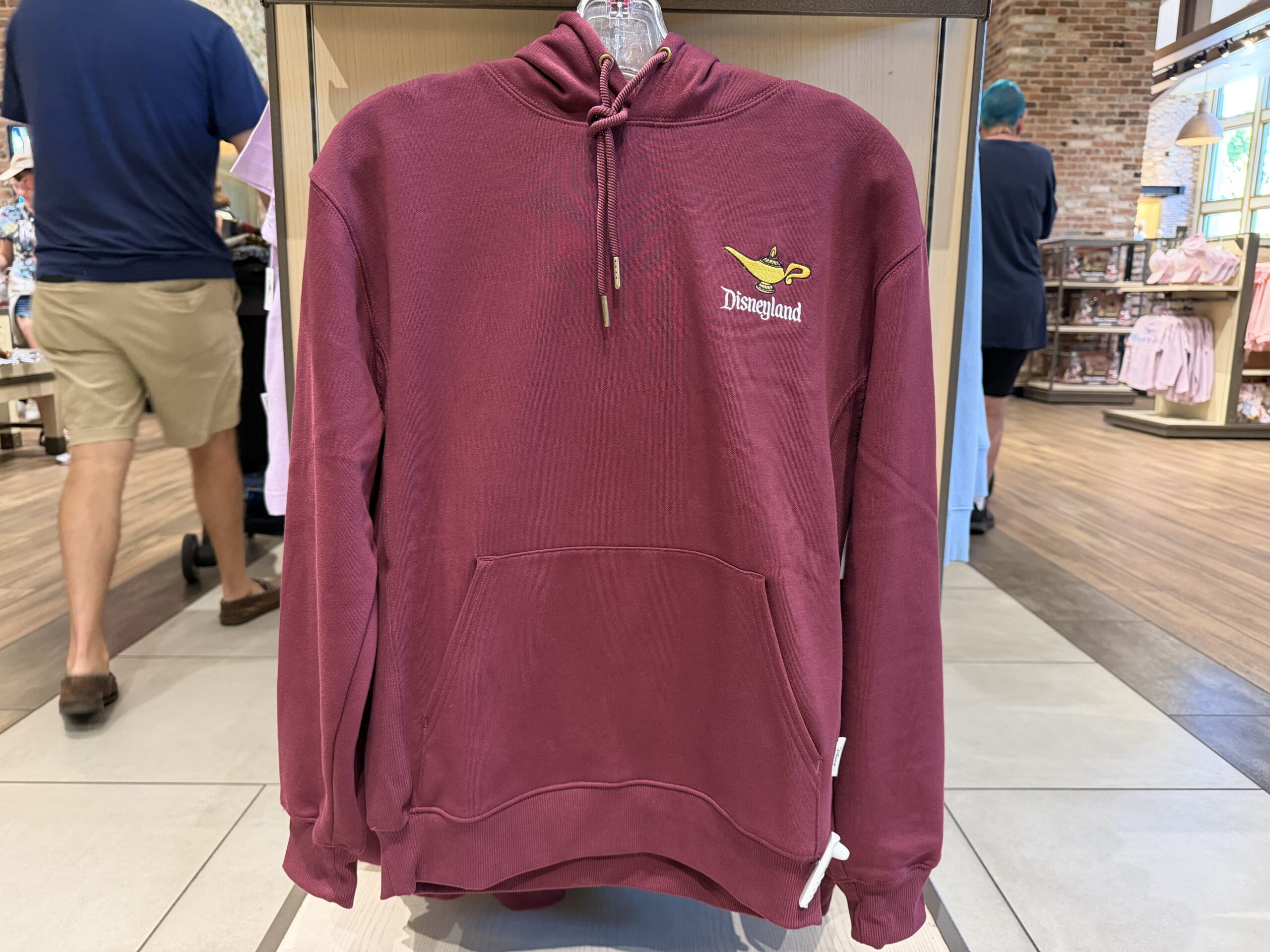 The hoodie is a rusty red. It has a drawstring hood and kangaroo front pocket. Embroidered on the left chest is Genie's lamp and "Disneyland."