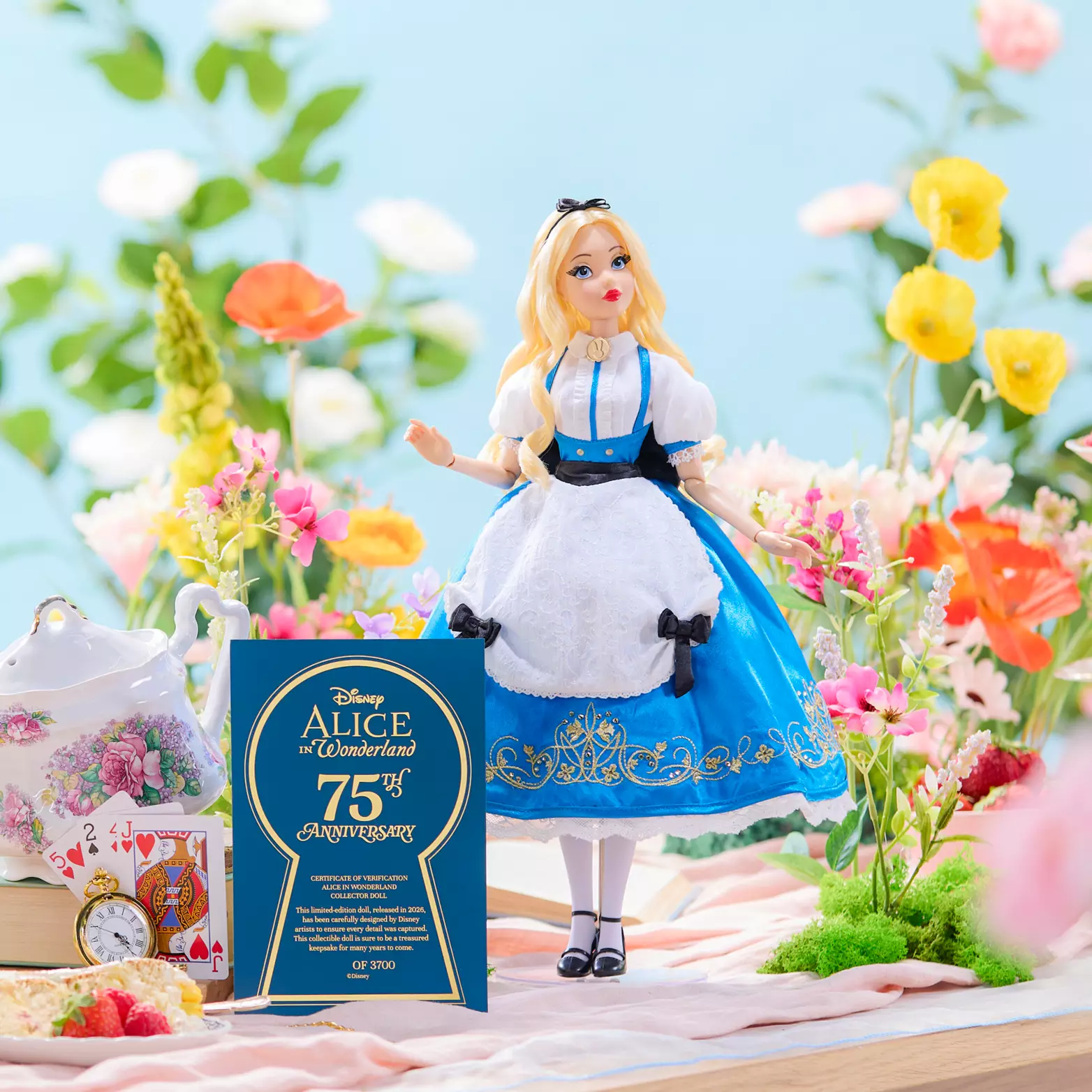 The limited-edition Alice doll wears a highly detailed couture version of her usual blue-and-white dress. This one has gold scrollwork near the bottom of the skirt and black bows along the apron and the waist. She has cherry-red lipstick, large eyelashes, and long, curled blond hair.