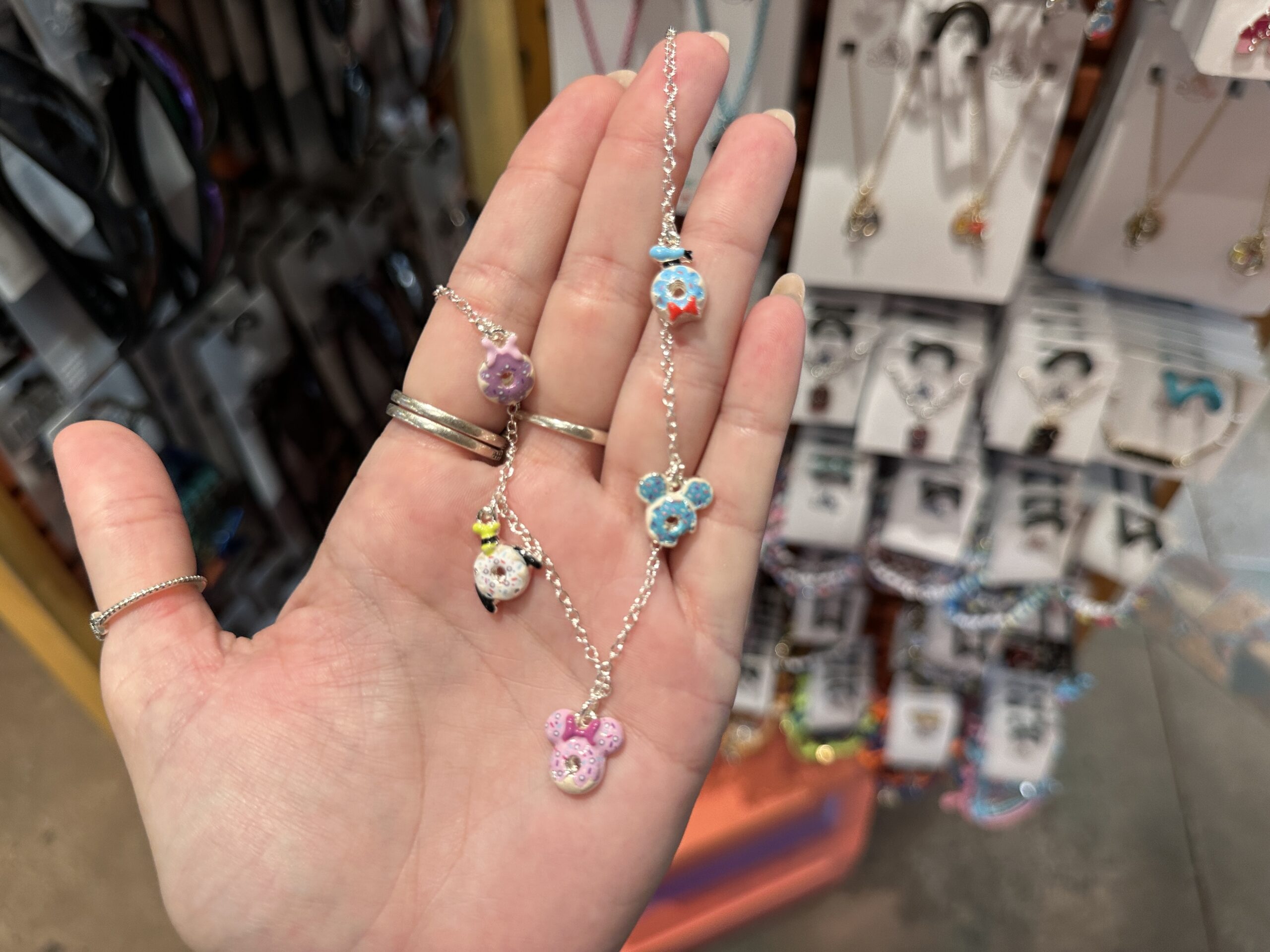 This long necklace has five small charms on it, each icon representing a different Disney character as a donut. It shows Daisy, Donald, Mickey, Minnie, and Goofy all in pastry form.