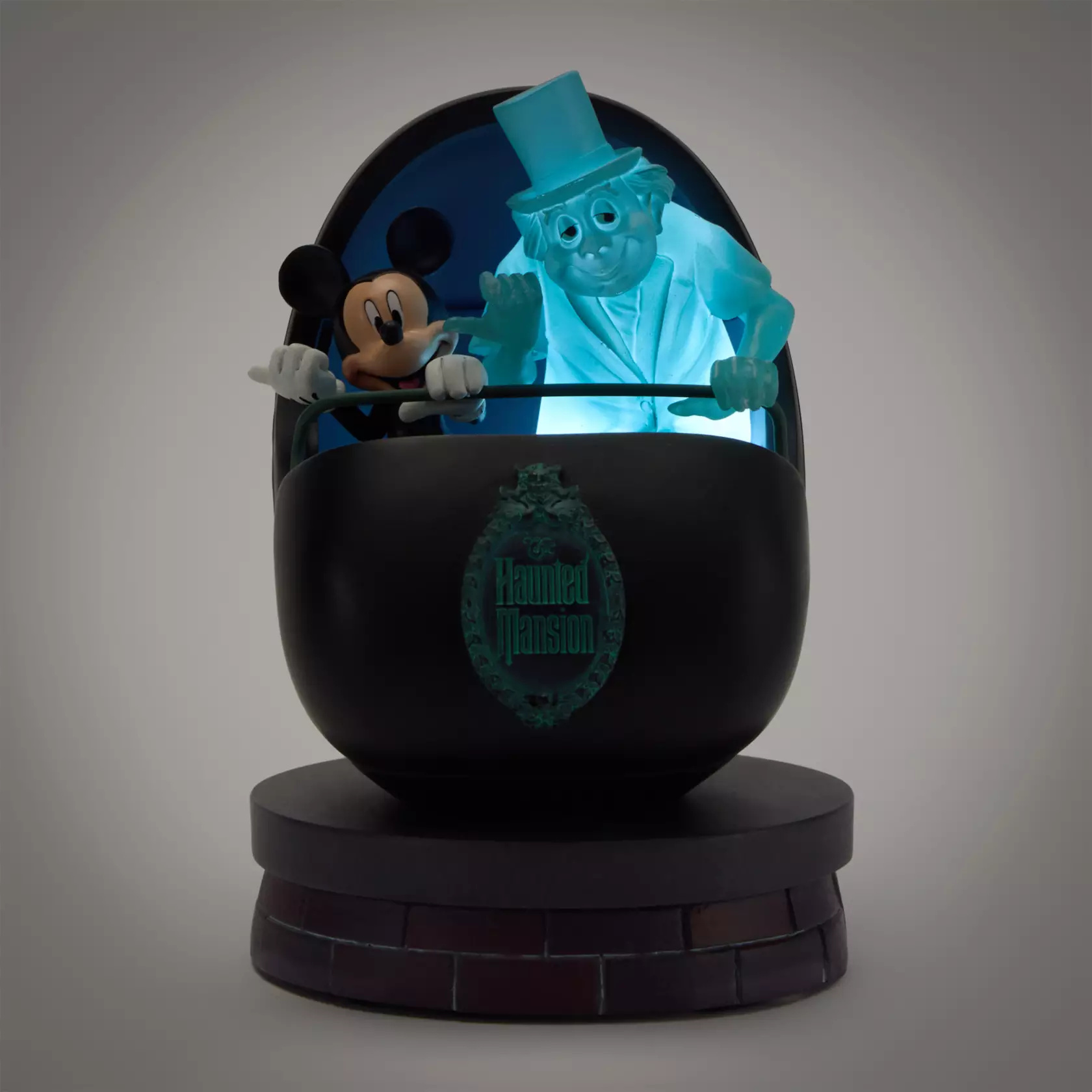 Mickey Mouse is depicted in a Doom Buggy alongside Phineas the Hitchhiking Ghost. The sculpted resin figure is 5.5" tall. Phineas is translucent blue and lights up from within. The Haunted Mansion plaque is on the front of the buggy and it sits on a faux brick base.