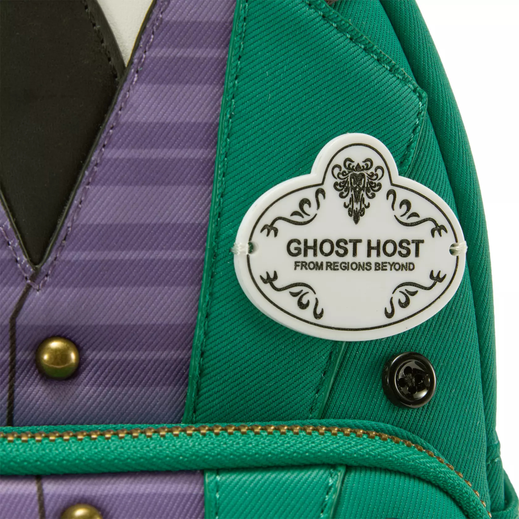 This backpack is inspired by the butler costumes worn by Haunted Mansion Cast Members. Appliqués and button details create the look of a green jacket over a purple striped waistcoat, black tie, white shirt, and dark green pants. A nametag on the front features wallpaper-inspired filigree around "Ghost Host - From Regions Beyond."