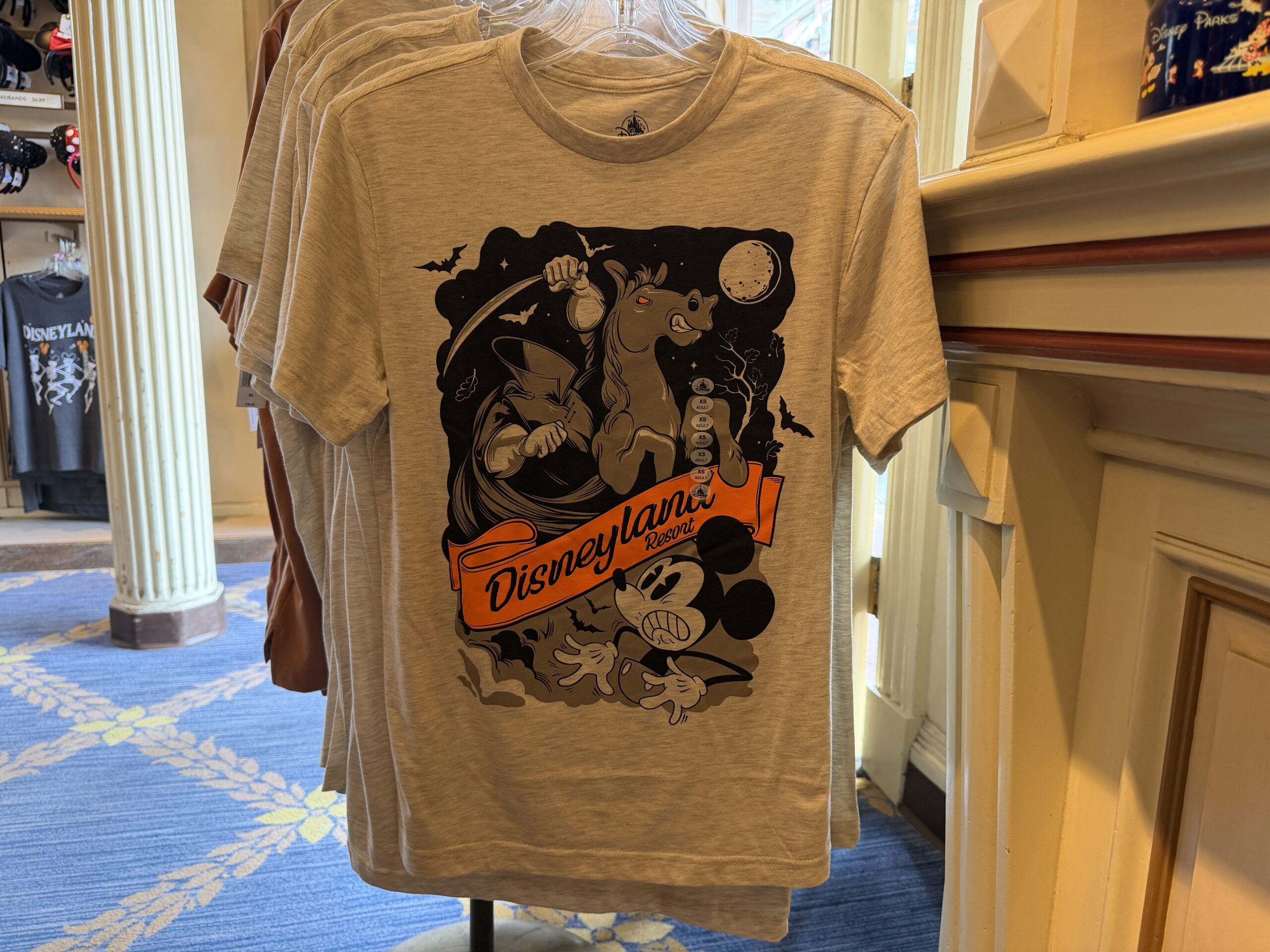 In heather gray, this shirt shows Mickey being scared by the Headless Horseman. The design is black and gray except for the bright orange “Disneyland Resort” ribbon in the center that matches the horse’s eye.