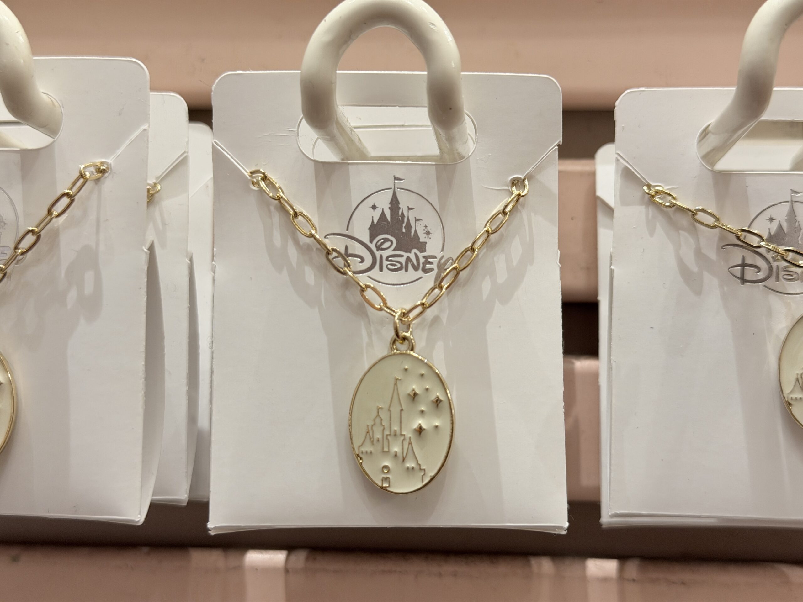 This cream-colored castle pendant comes on a gold-tone chain. It shows a Fantasyland Castle in a gold outline with shining gold stars to the right of it.