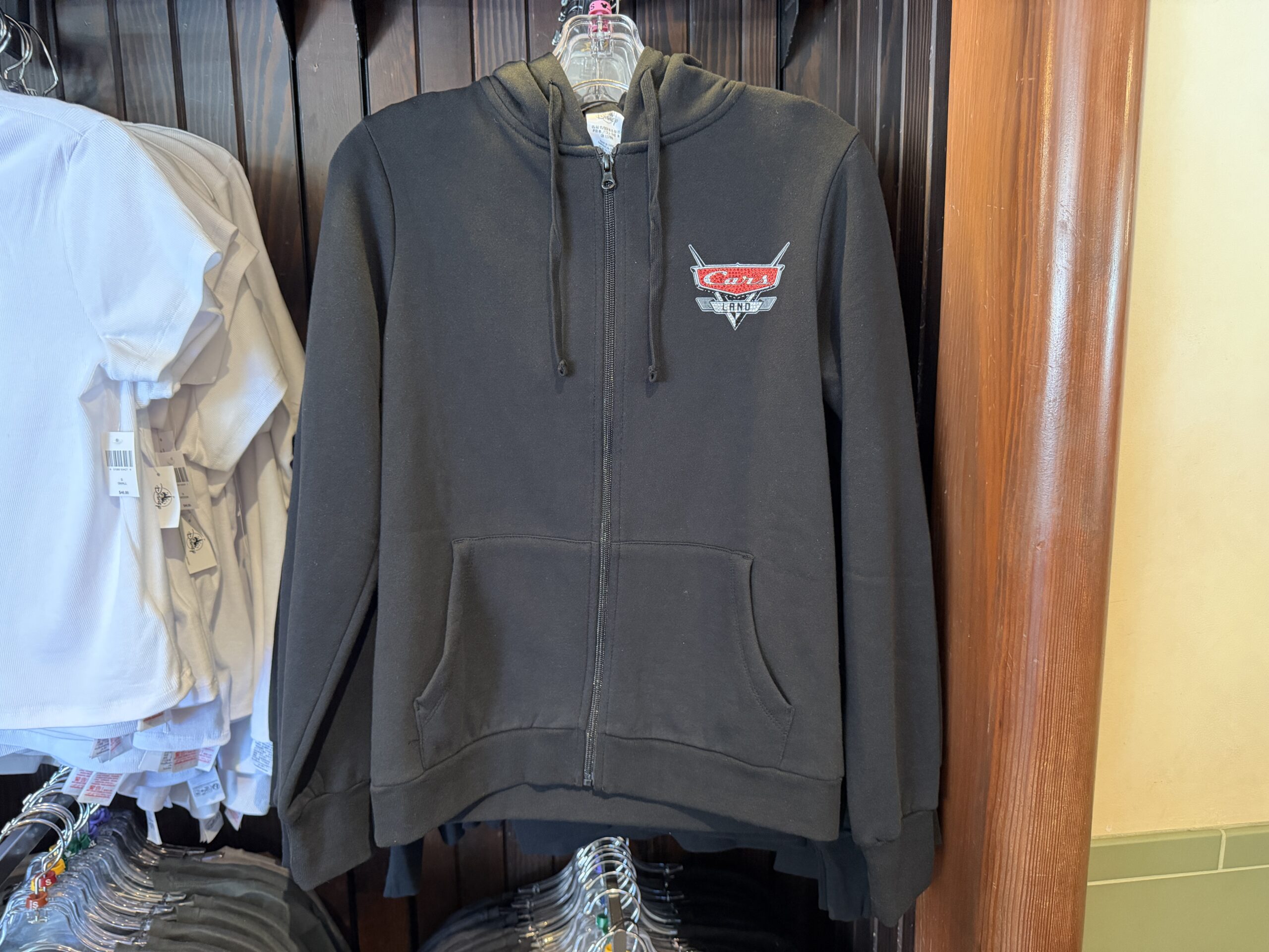 The black zip-up hoodie has a front pocket. On the chest is the Cars Land logo in black, white, and red. Most of the logo is bedazzled.