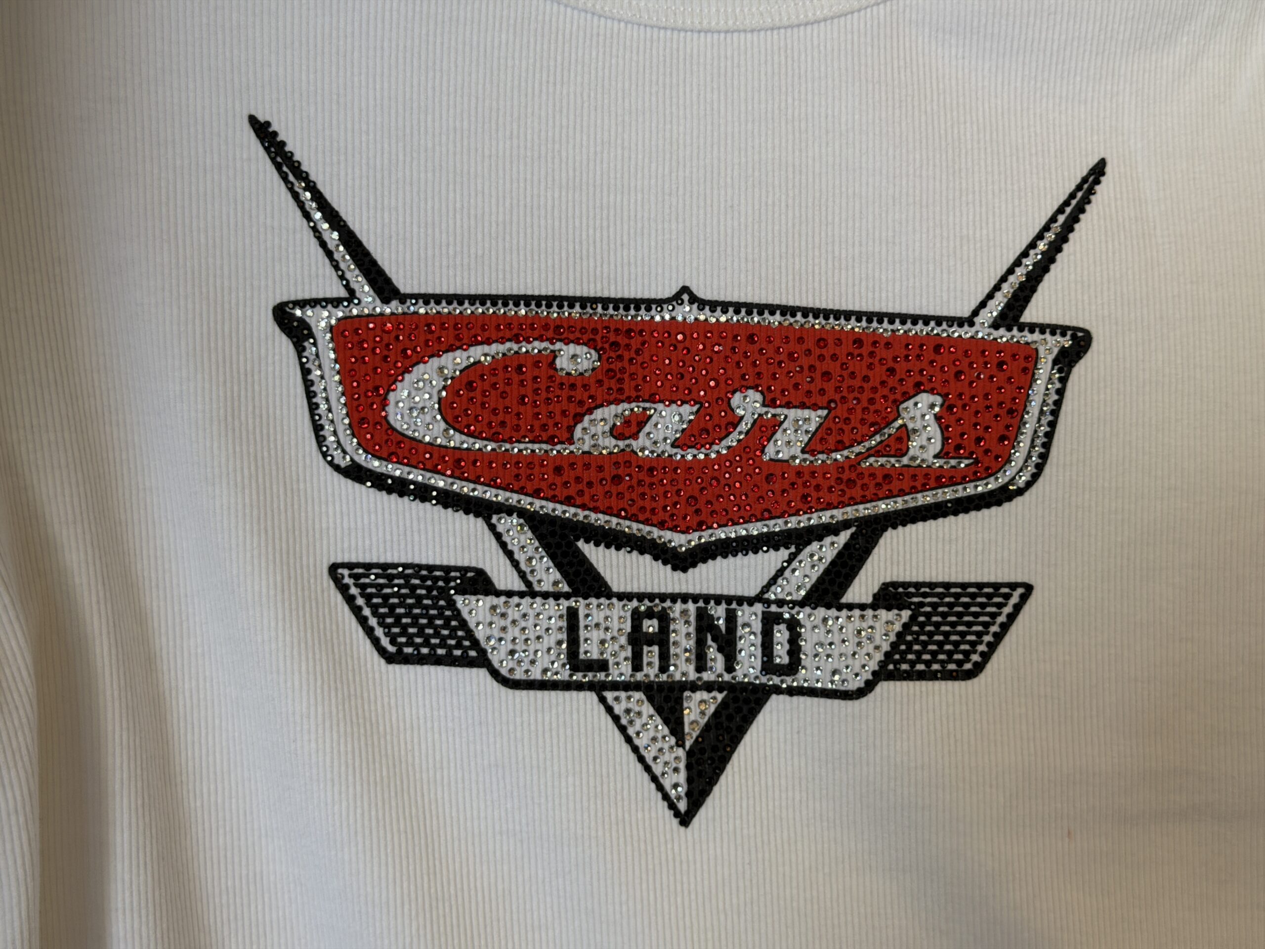This white tee has a large bedazzled logo in the center of the chest. The back is plain.