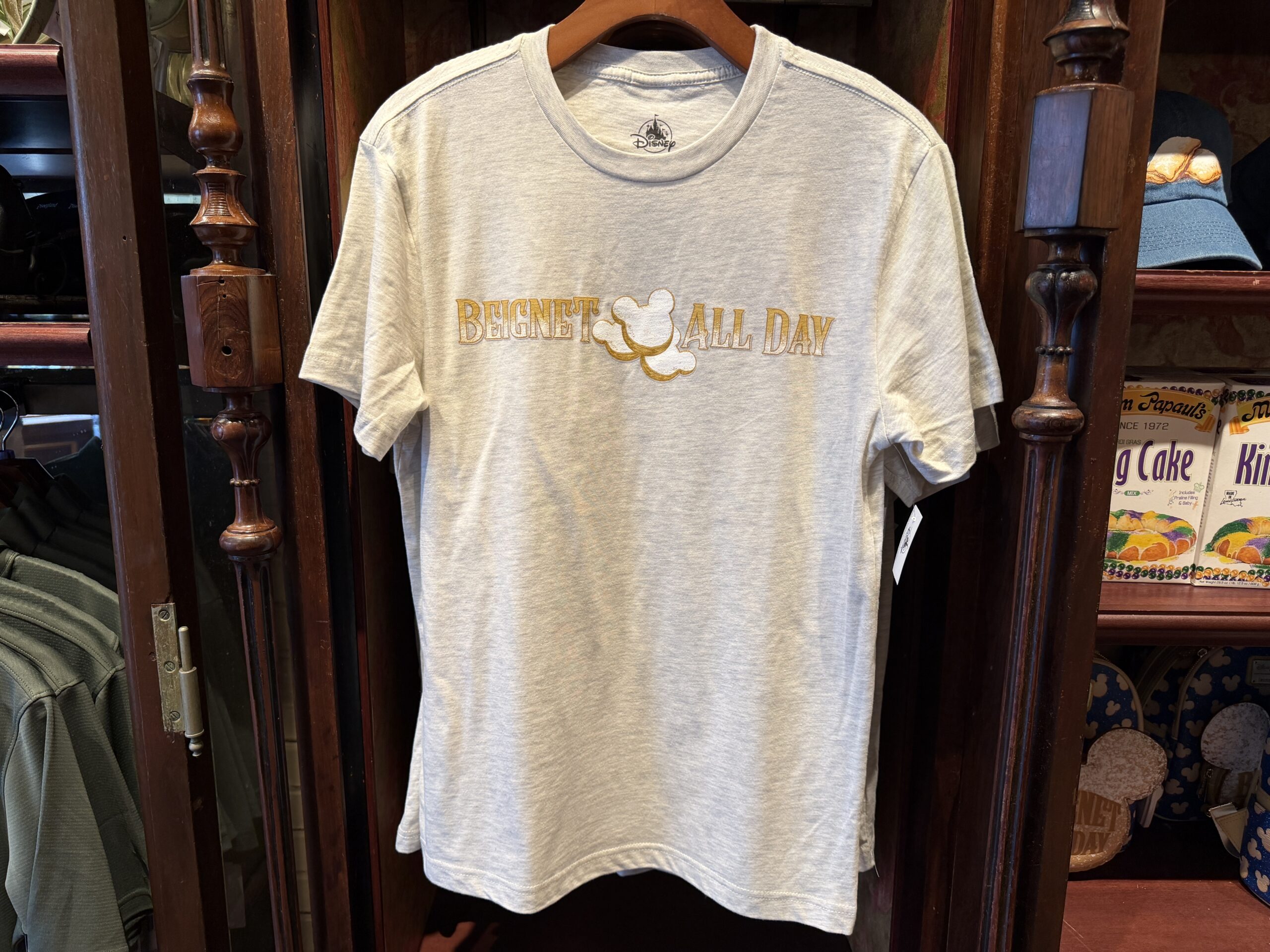 The gray T-shirt has "beignet all day" text in ombre dusted beige and white text. Three beignets are placed in the center with powdered dusting.