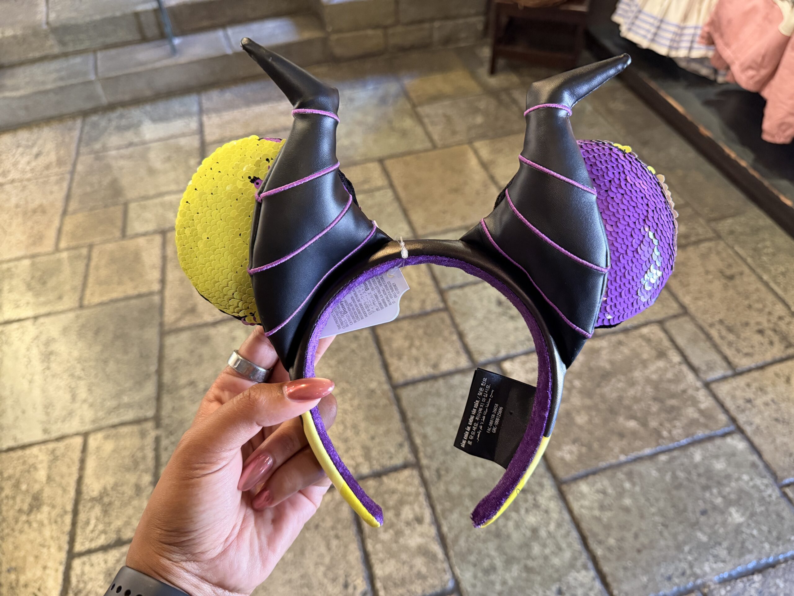 These ears are covered in reversible purple and green sequins. Black faux leather horns with purple piping details sit on the band in front of the ears.