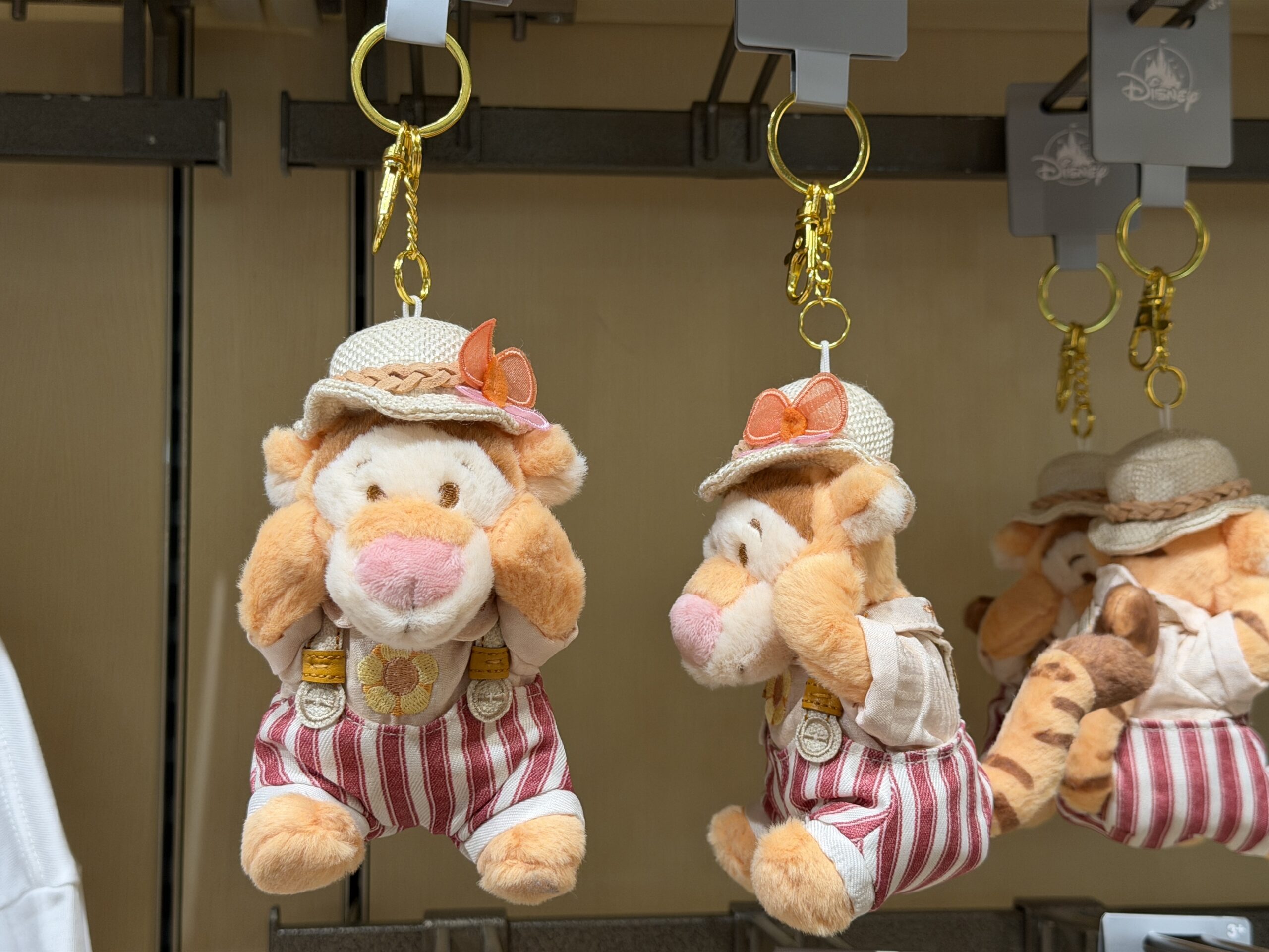 The tigger plush is also on a goldtone keychain. Tigger wears striped pants, suspenders, and a shirt featuring a yellow flower.