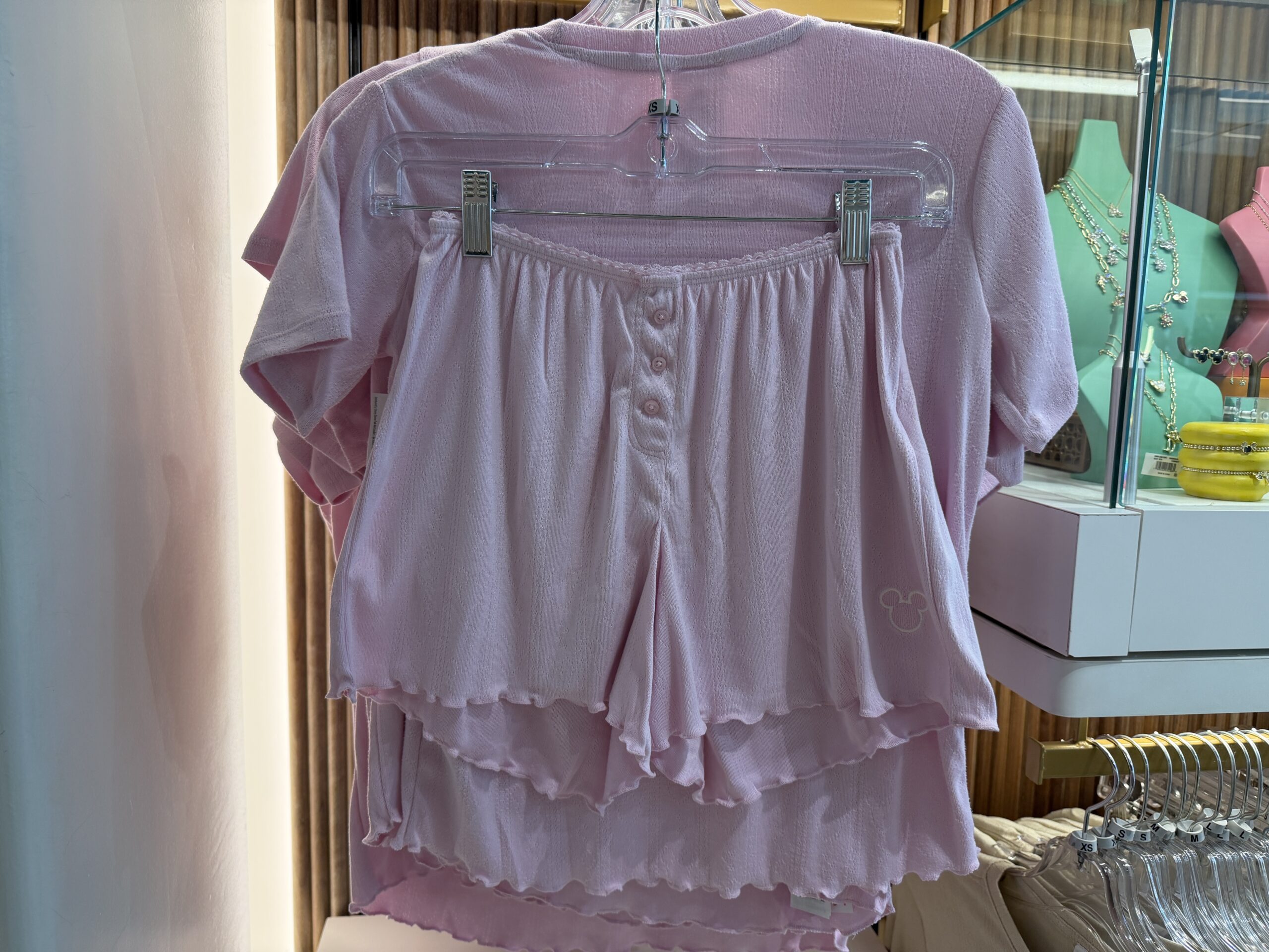 With a ruffled waist and leg hems, this two-piece sleep set comes with matching shorts and T-shirt. They are both in light pink, and the top has a small, white Mickey head icon on the left side of the chest.