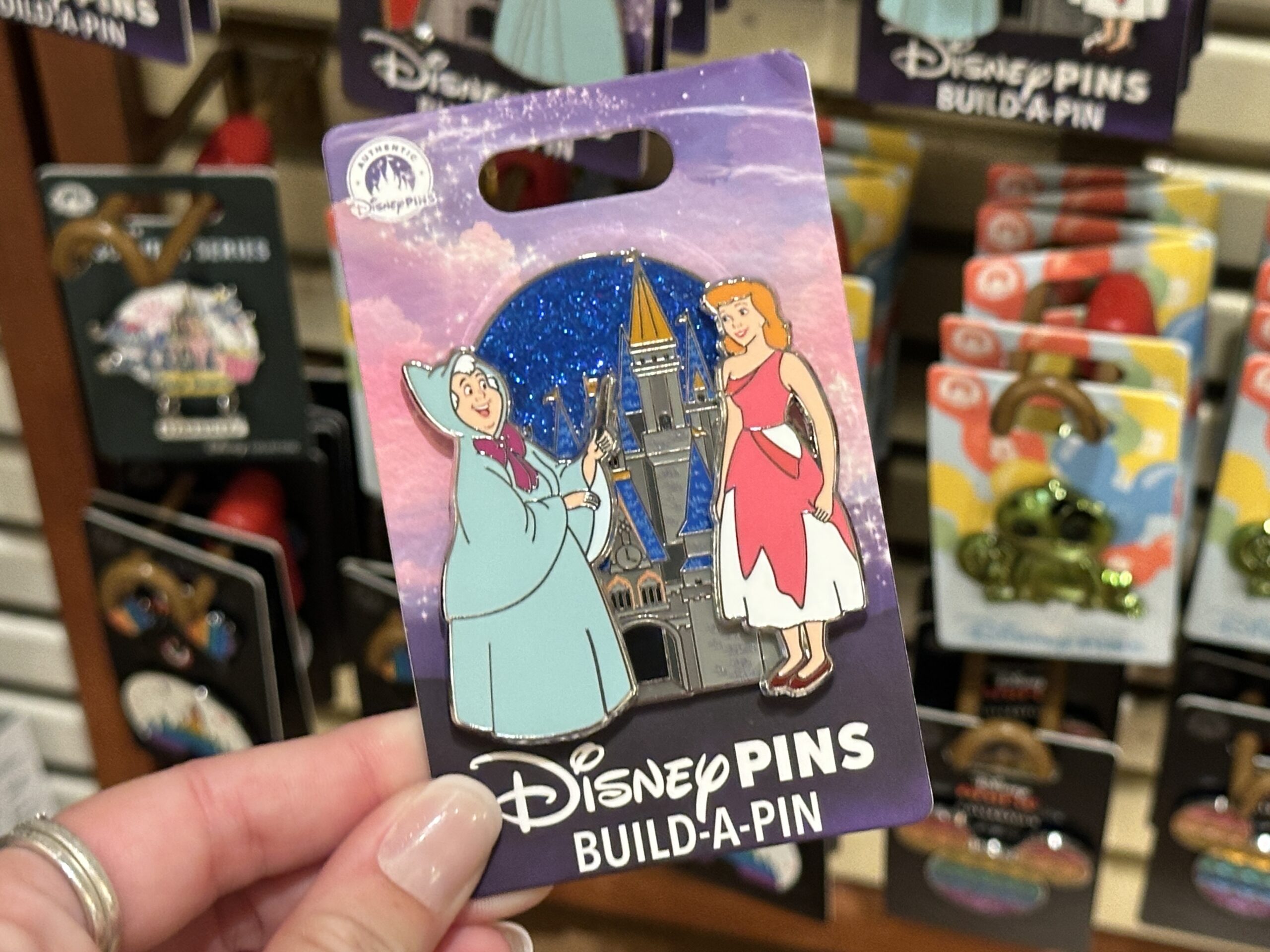 This set includes the base pin, which features Cinderella Castle against a blue sparkly background. The two pins that attach depict the Fairy Godmother and Cinderella in her tattered pink dress.