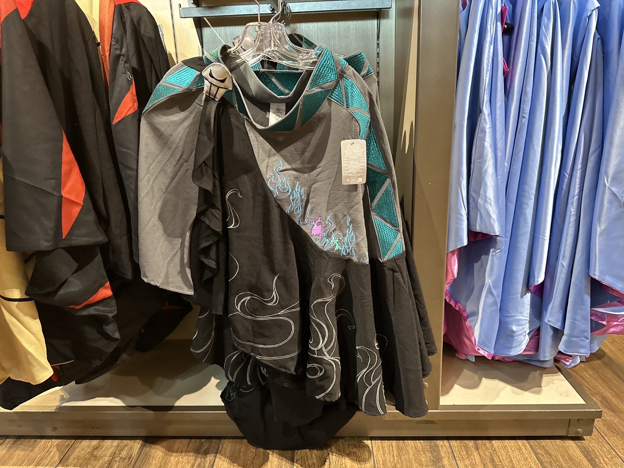 Representing Hades, this cape shows the Underworld-dwelling ruler’s henchmen Pain and Panic as embroidered characters on the skirt jumping through blue embroidered flames. It is primarily grey and black with a blue geometric belt with an applique of a skull like Hades’ toga accessory.