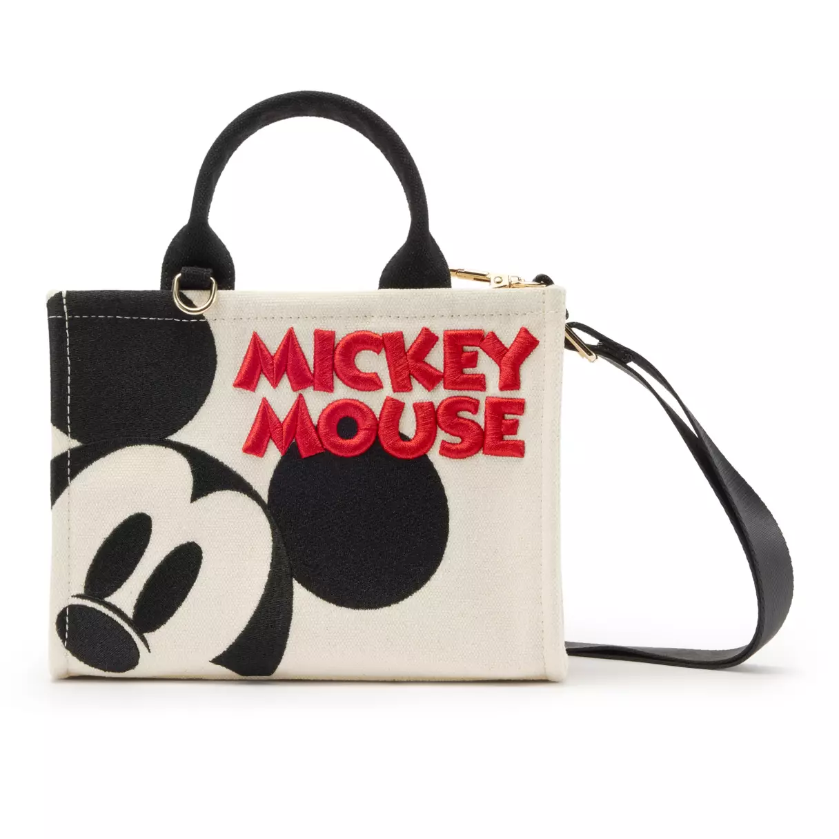 A canvas tote featuring Mickey Mouse is also available. The tote is ivory with Mickey peeking out from the side in black. His name is prominently displayed on the front as well in bold, red letters. The back of the tote is blank.