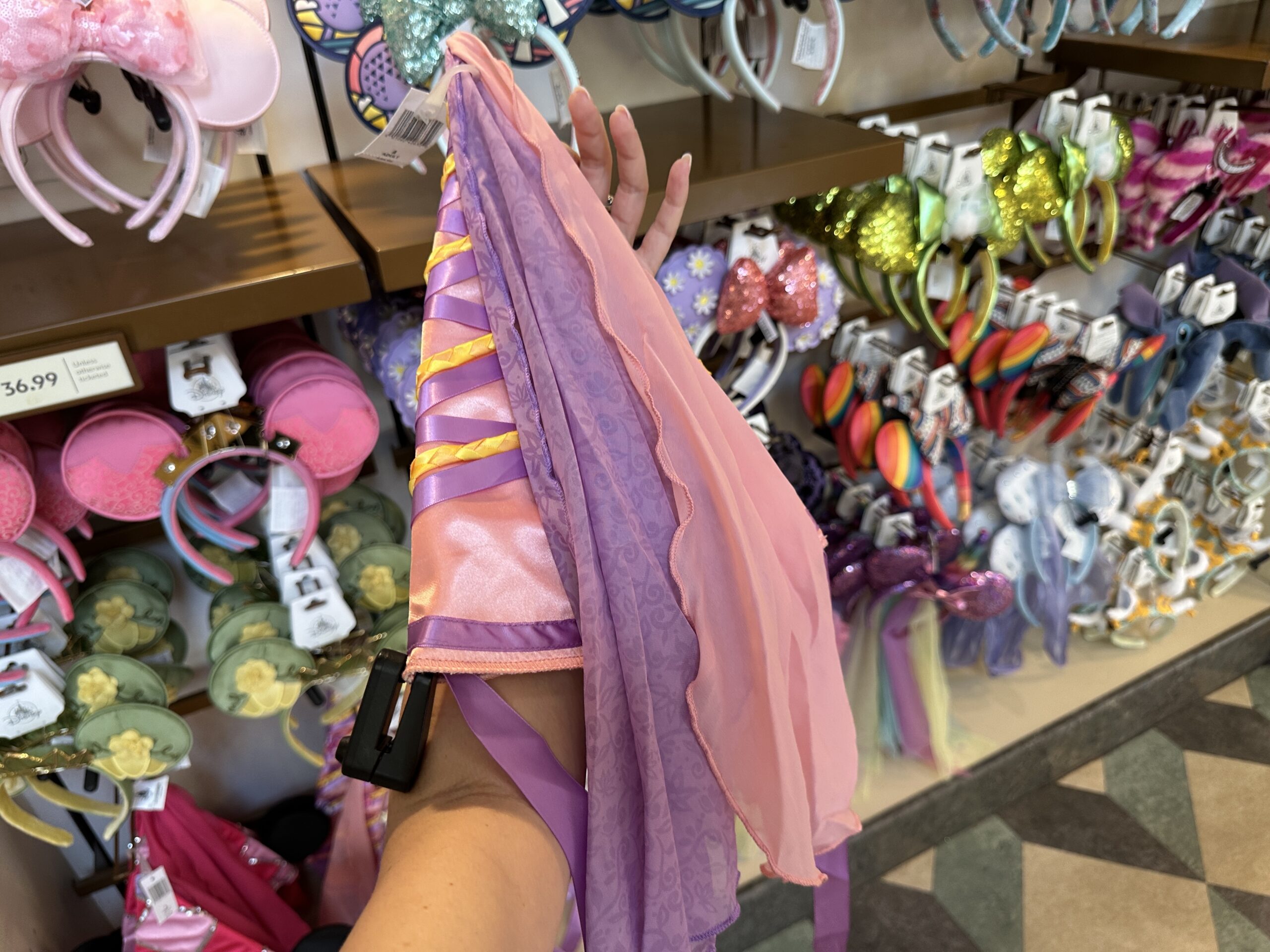 On the back of the hat, two handkerchief-esque tulle pieces of fabric hang down. One is a plain light pink while the other is purple with a floral and filigree pattern on it.
