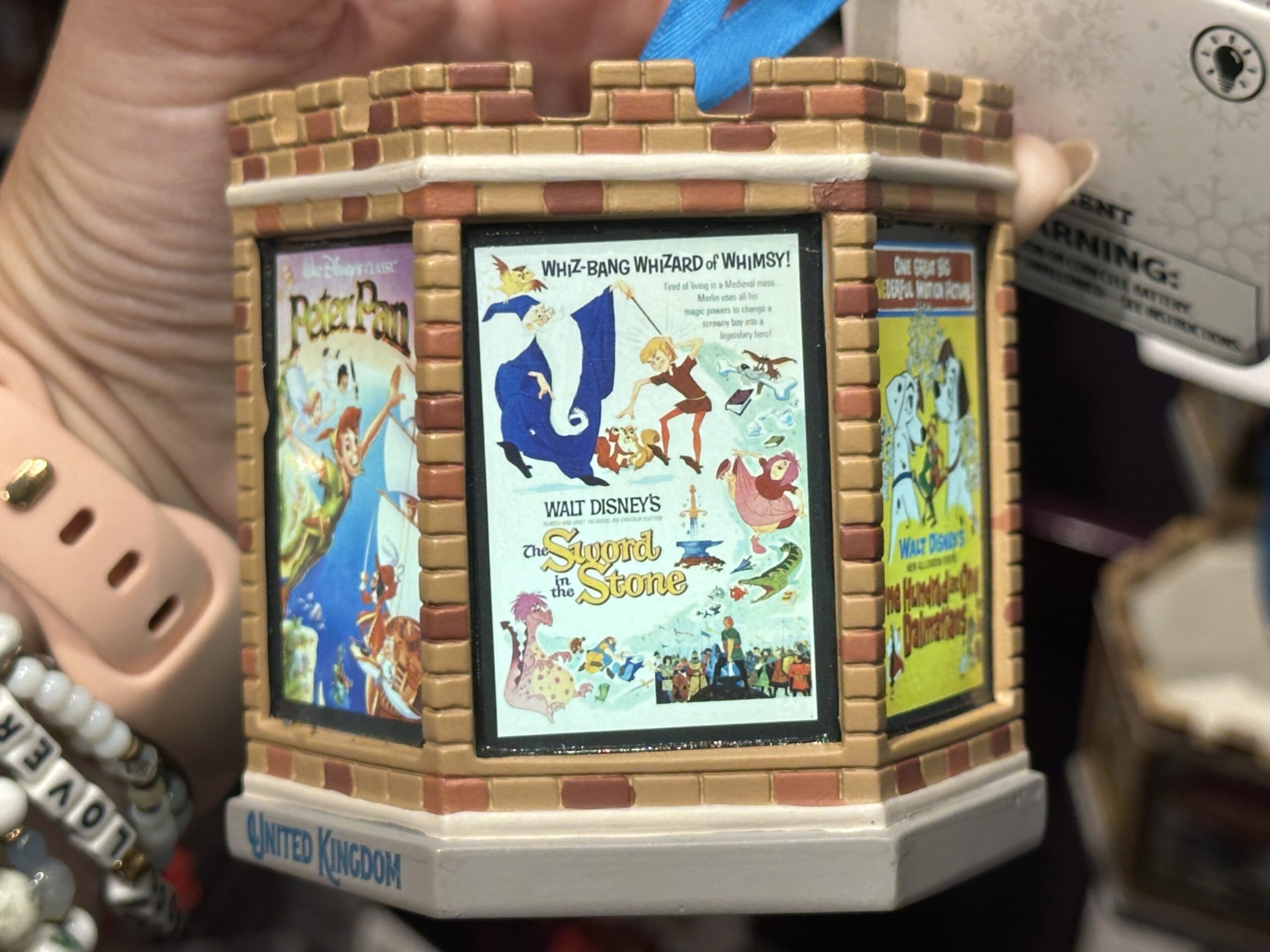 This six-sided, light-up ornament celebrates classic Disney films that took place in England. Each side has a different vintage poster from the film. These include Peter Pan, The Sword in the Stone, One Hundred and One Dalmatians, Icabod and Mister Toad, Alice in Wonderland, and Robin Hood. The ornament is designed like the top of a castle tower.