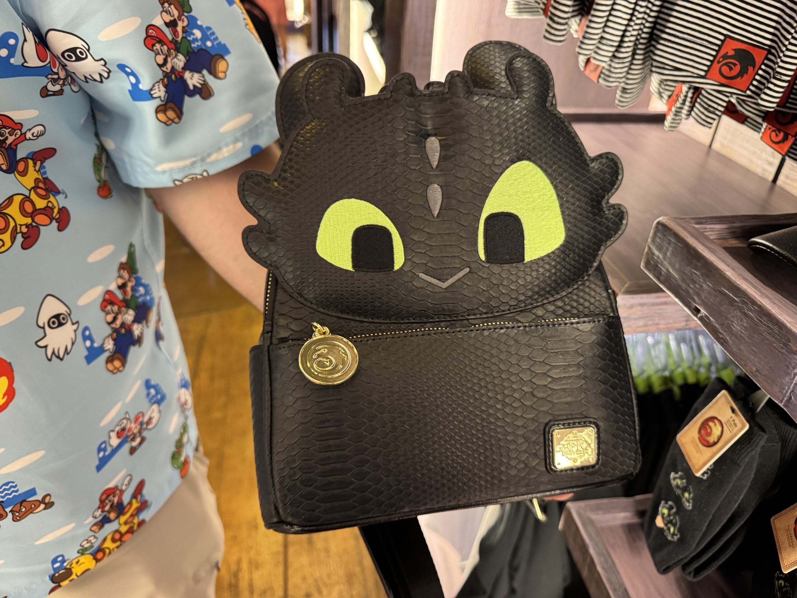 This glow in the dark Loungefly mini backpack is black with textured dragon scales to mimic Toothless. His face is at the top on the front, and the Epic Universe logo is in the bottom corner.