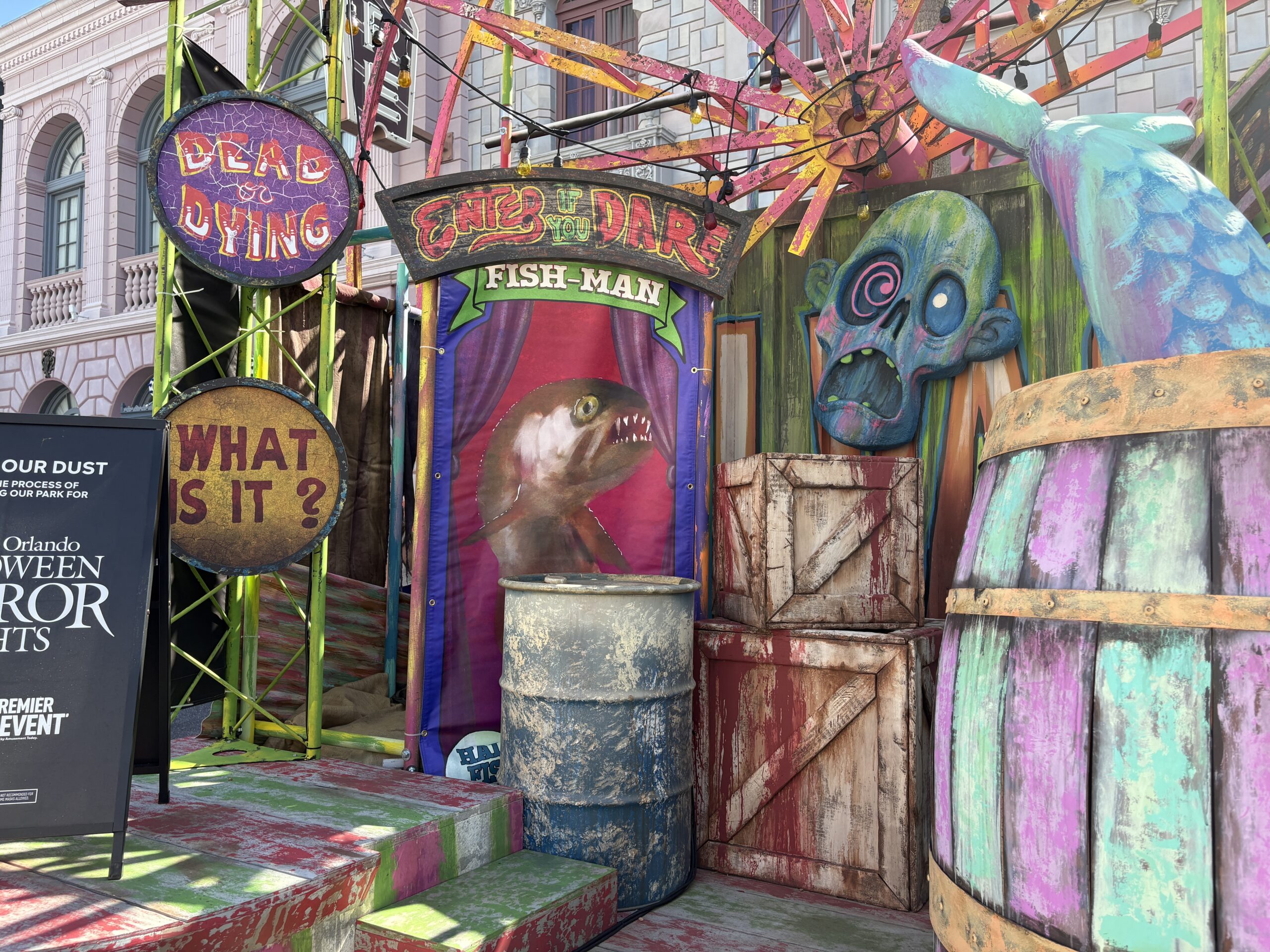 A banner at the back advertises a Fish-Man under an "Enter if you Dare" sign. Two crates appear to be seeping blood. Other signs read "Dead or Dying" and "What is it?"