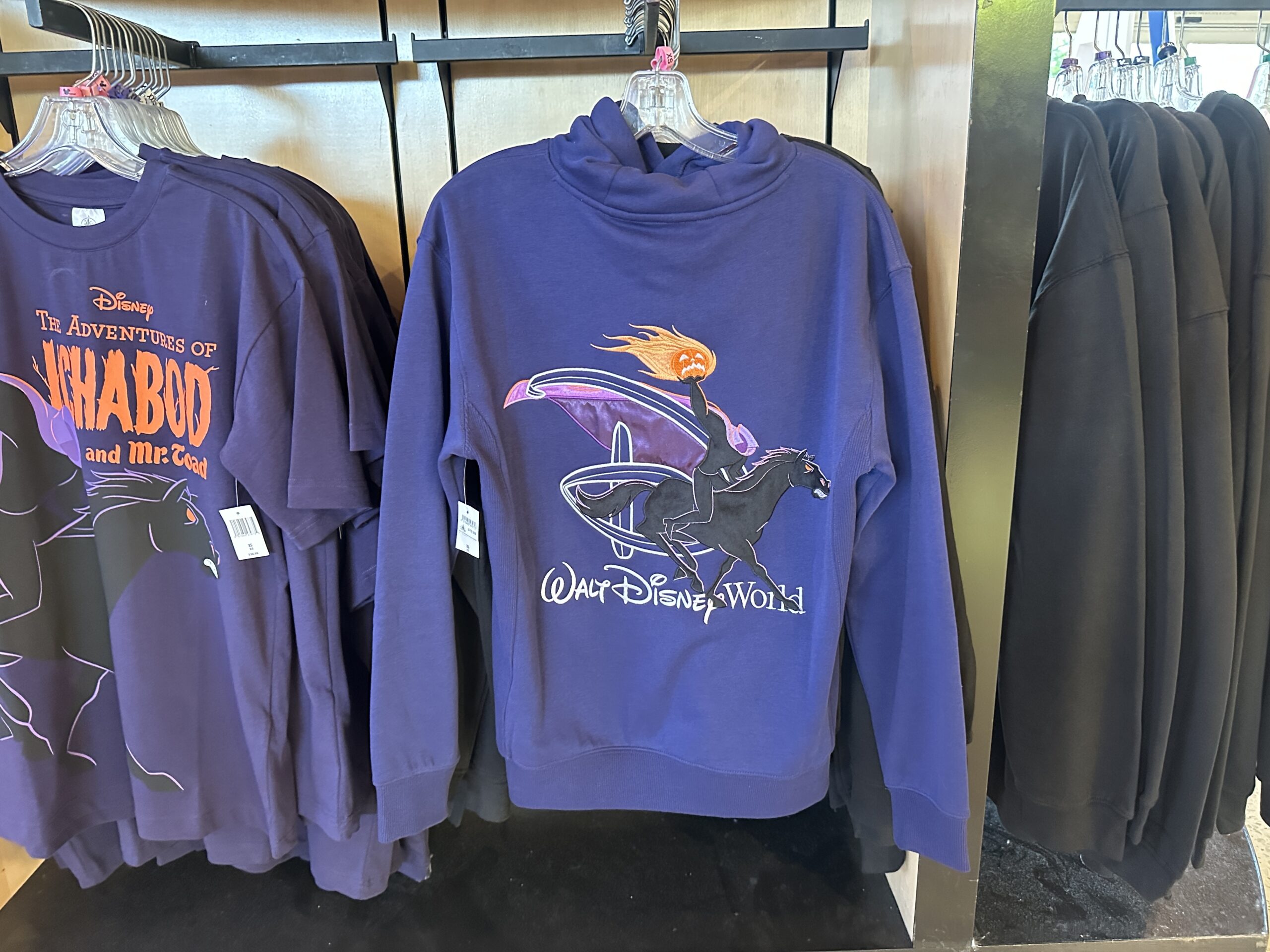 This purple hooded sweatshirt has a kangaroo pocket and the flaming pumpkin with the WDW wordmark on the front. On the back is a larger image of the Headless Horseman holding the pumpkin. A "D" is behind him, and the Walt Disney World wordmark is under him.