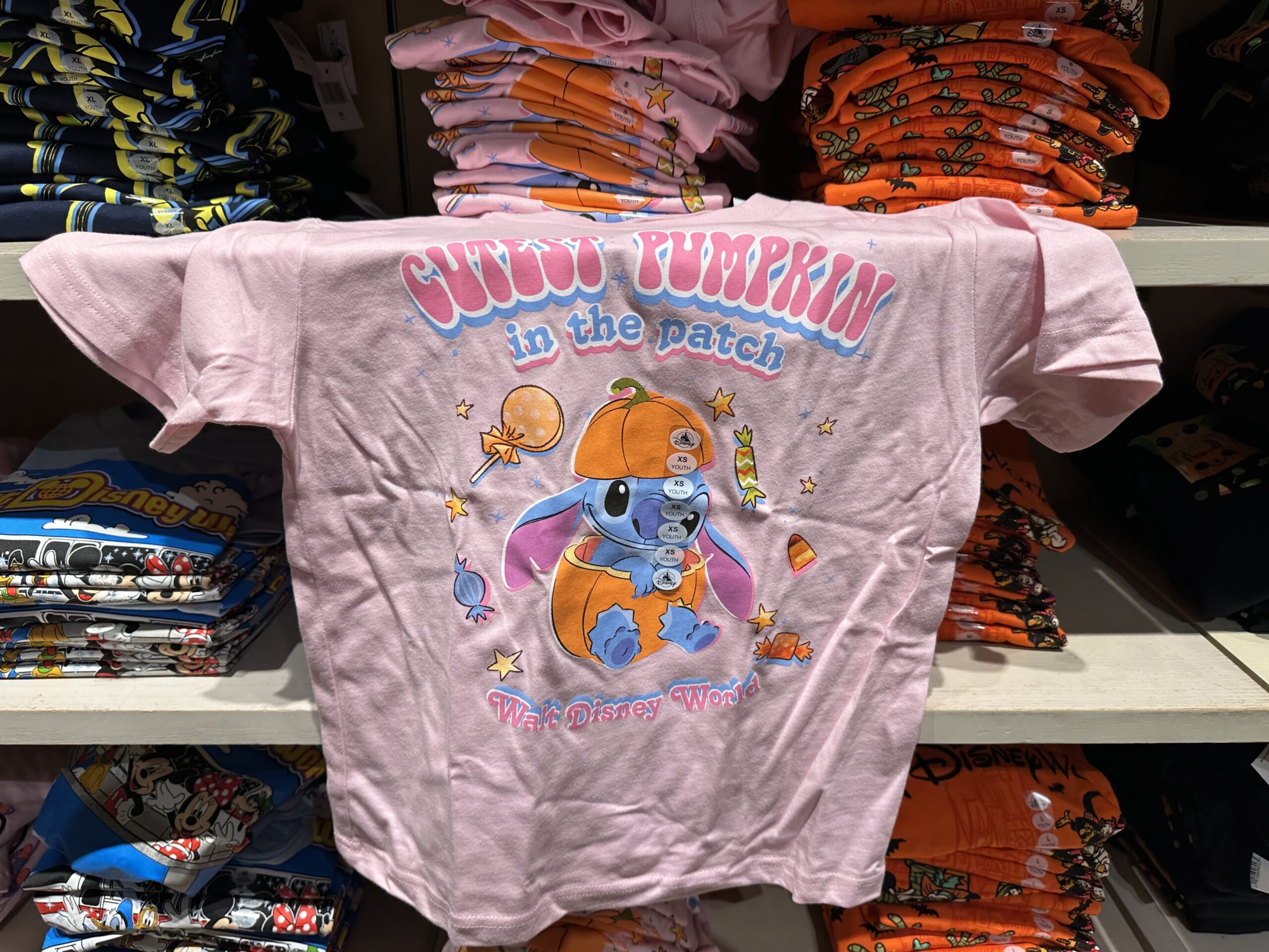 Stitch sits inside a pumpkin on this pink tee as Halloween candy surrounds him. "Cutest Pumpkin in the patch" is at the top in pink and blue text. "Walt Disney World" is at the bottom in the same style.