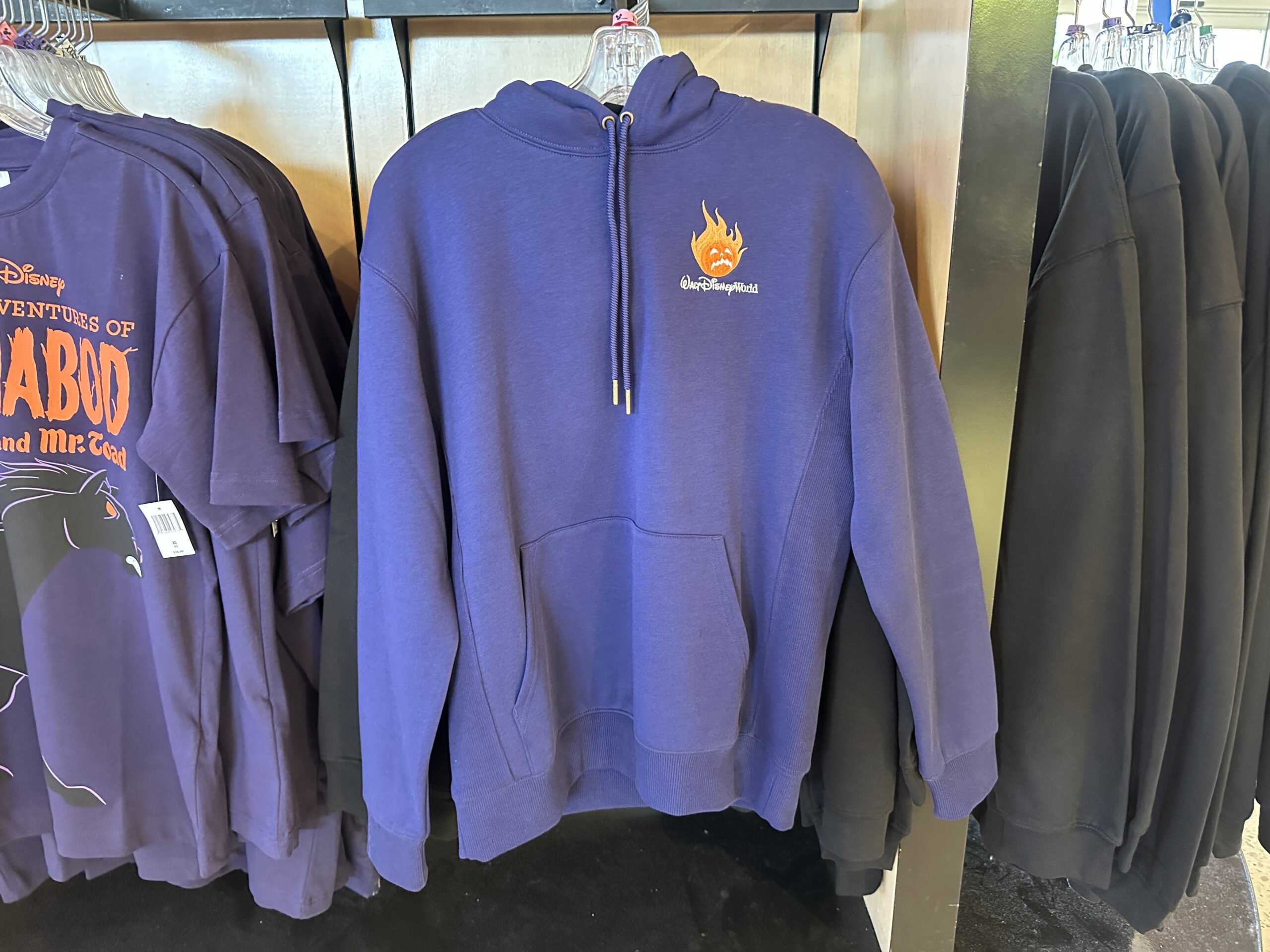 This purple hooded sweatshirt has a kangaroo pocket and the flaming pumpkin with the WDW wordmark on the front. On the back is a larger image of the Headless Horseman holding the pumpkin. A "D" is behind him, and the Walt Disney World wordmark is under him.