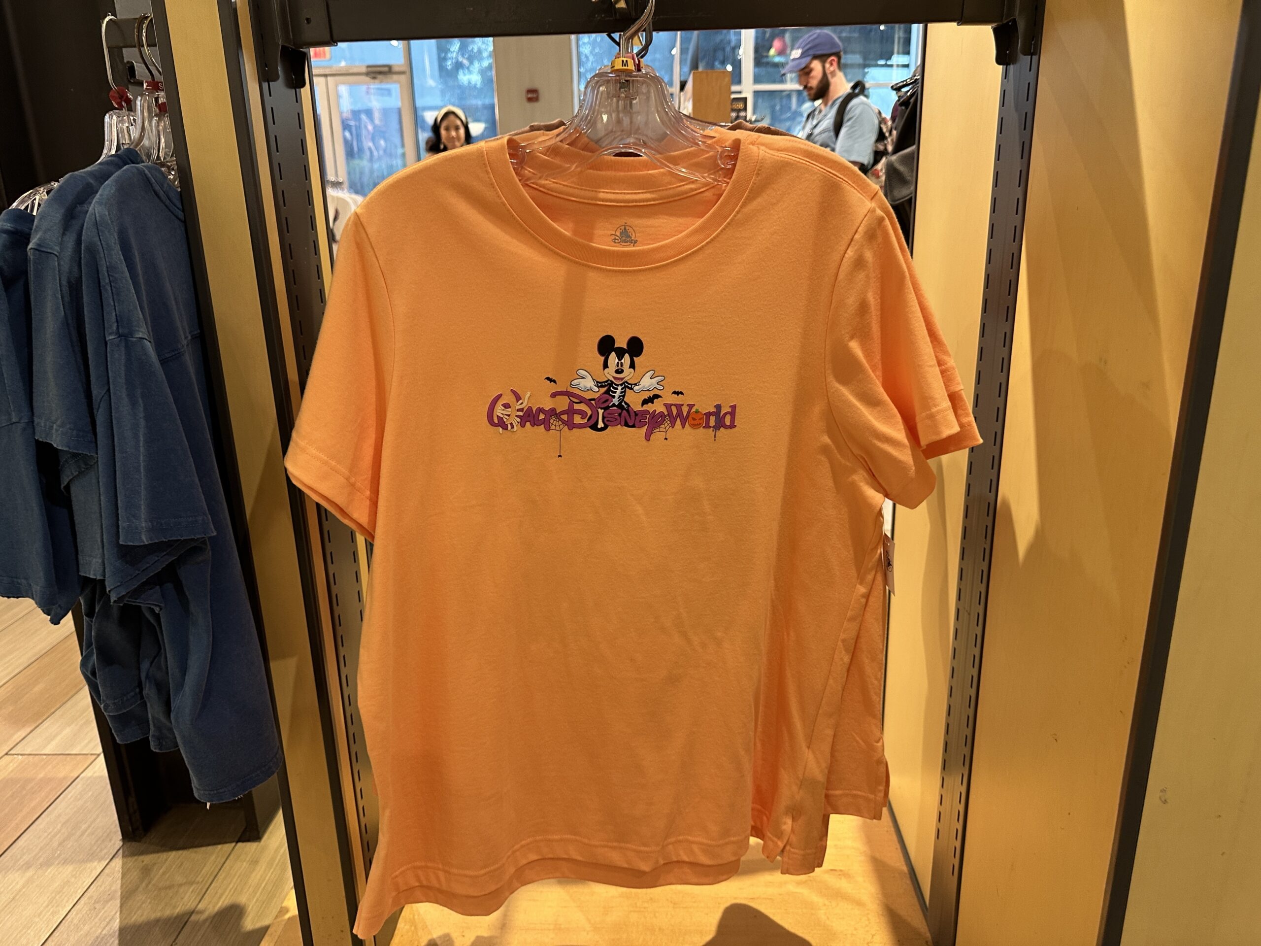 The orange tee has an image of Skeleton Mickey standing above the Walt Disney World wordmark, which is purple. On the back, Mickey and his friends stand around the words "Happy Halloween."