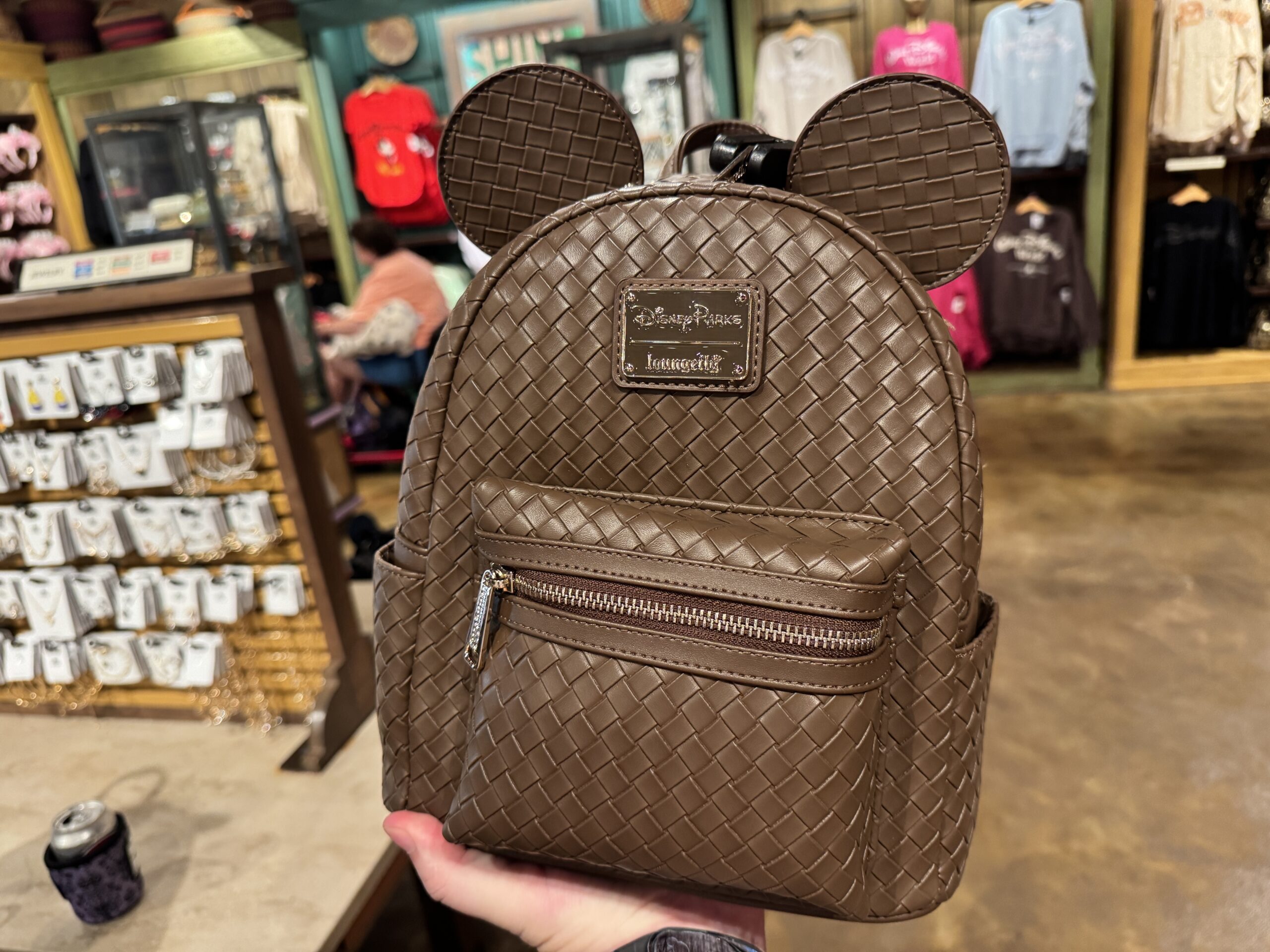 In the style of basket weaving, this brown Loungefly backpack is covered in the pattern, even the two Mickey ears on the top. It has an exterior pocket with a zipper on the front as well as a side pocket on either side of the bag.