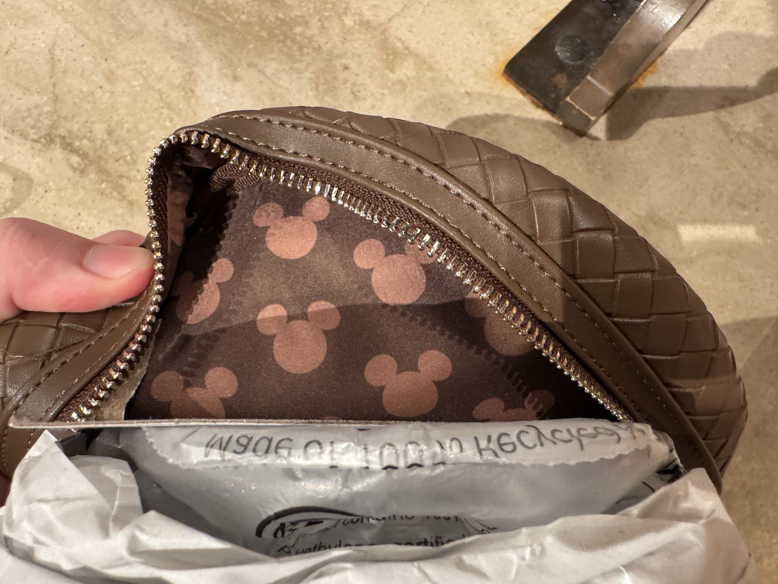 On the inside of the bag, the lining is the same shade of deep brown with a pattern of lighter brown Mickey head icons throughout.