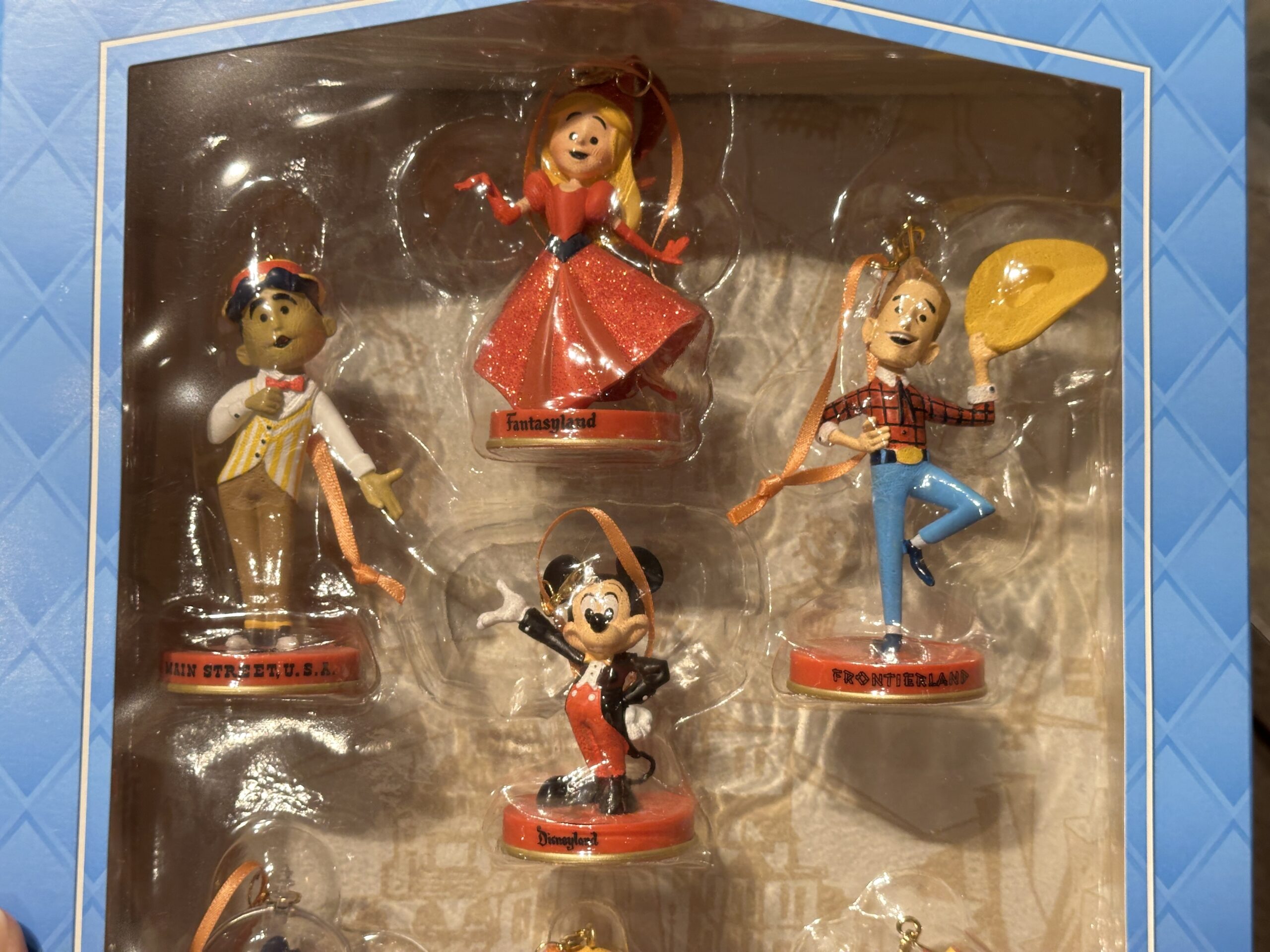 The Fantasyland character is a princess in red, the Main Street, U.S.A. character wears a pinstriped vest, and the Frontierland character is in a flannel shirt, jeans, and a cowboy hat.