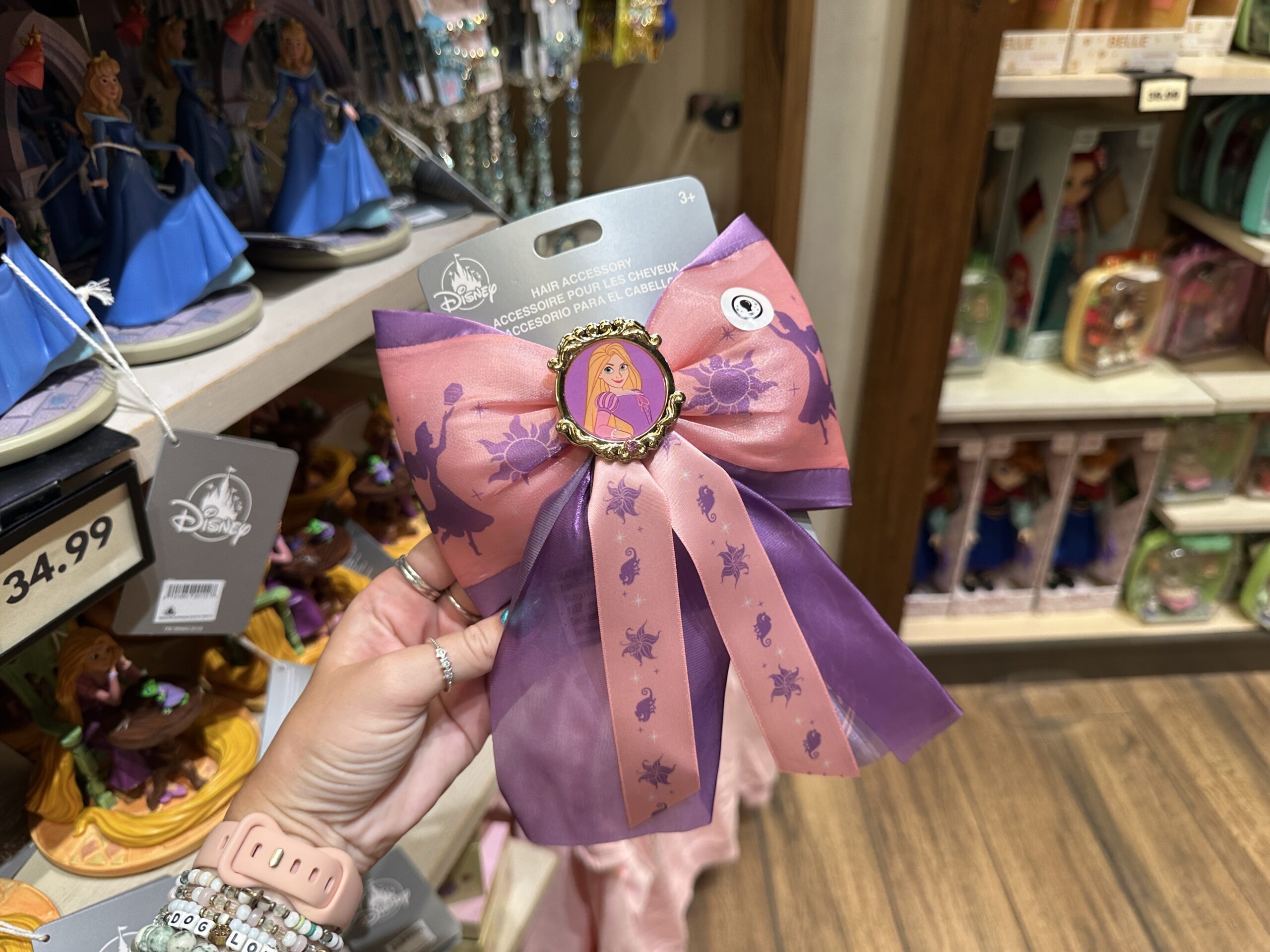 This pink and purple bow features Rapunzel in the center portrait, as well as silhouettes of the Corona sun and the princess reaching for lanterns.