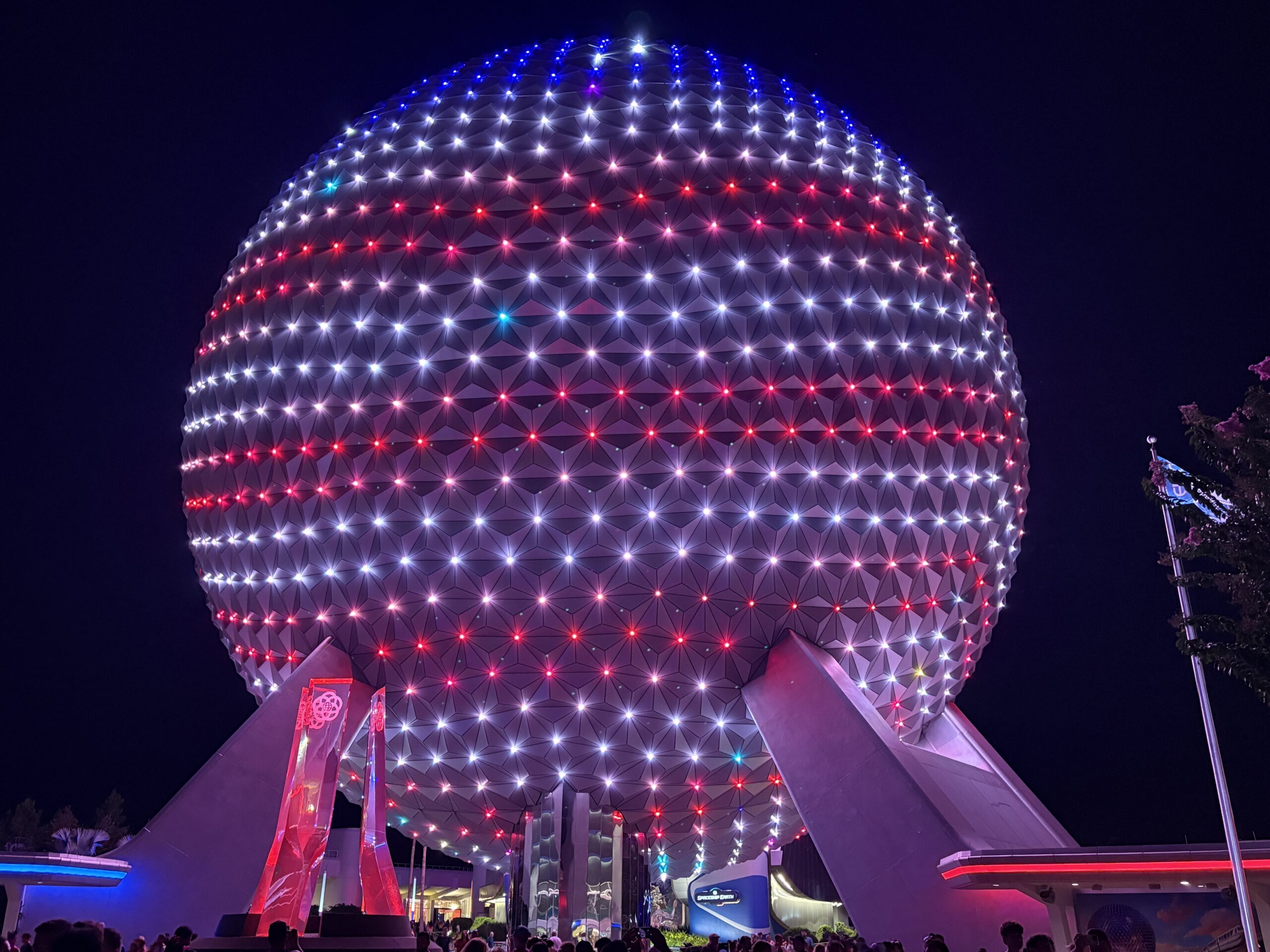 EPCOT has some patriotic lighting in place for America's 250th birthday this year. Spaceship Earth is decorated like an American flag, and other facades have red, white, and blue lighting.