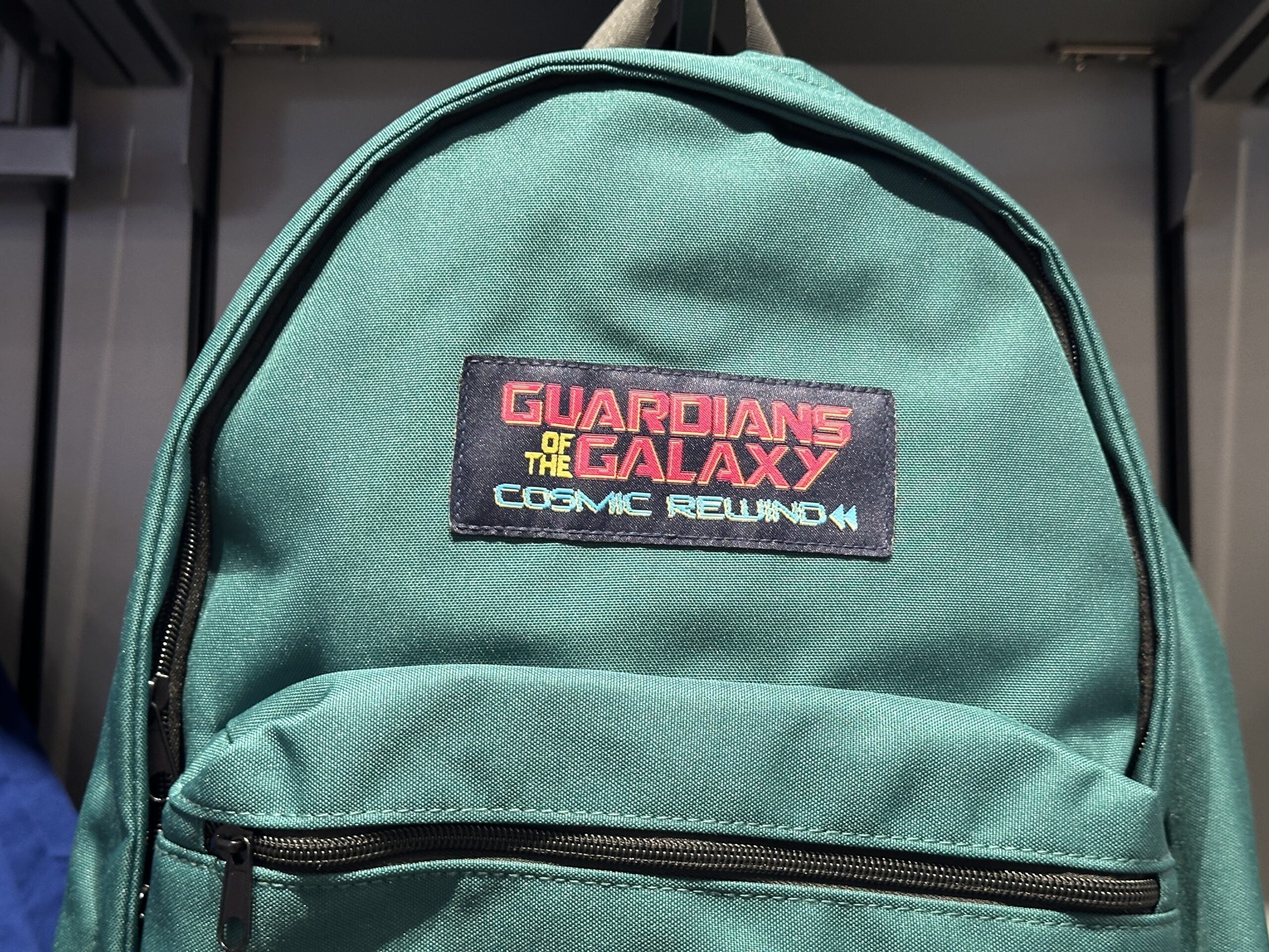 The green school-style backpack has a Guardians of the Galaxy: Cosmic Rewind patch above the front pocket. It has black zippers and a yellow base.
