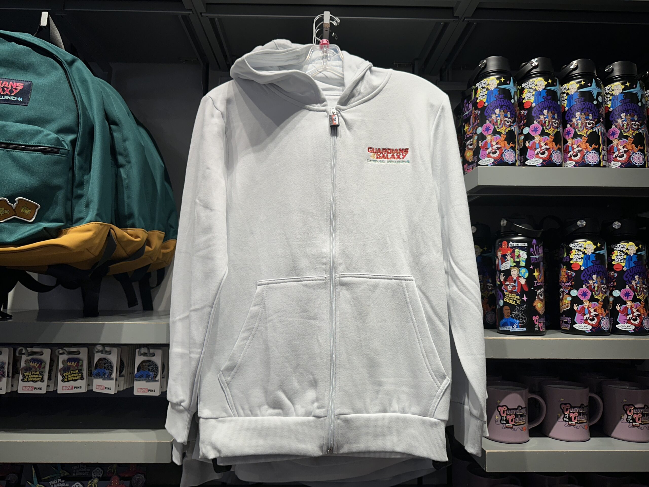 This white hoodie has kangaroo pockets and zips up with a silicone cassette tape zipper pull. The Guardians of the Galaxy: Cosmic Rewind wordmark is embroidered on the left chest.