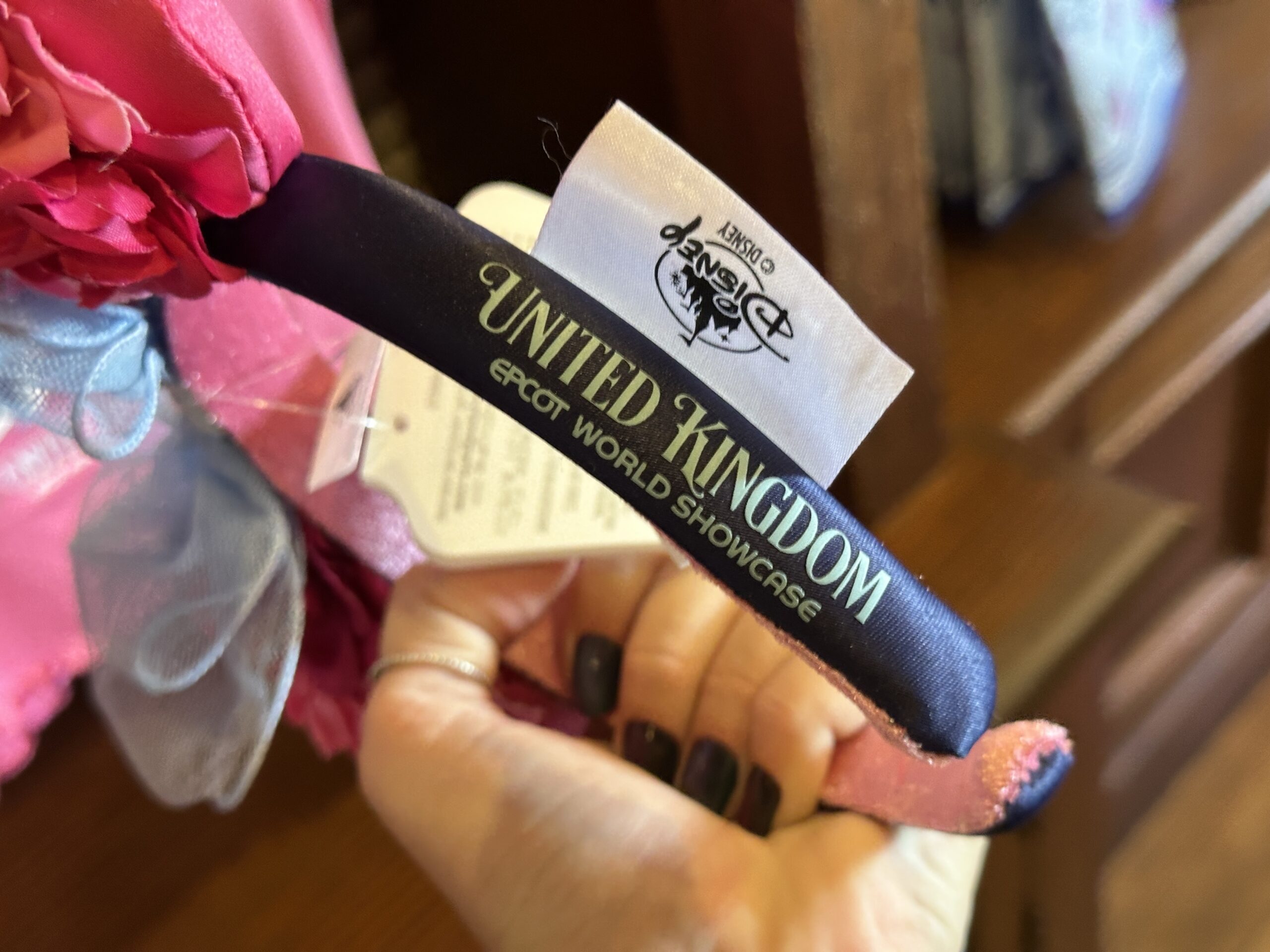 The backs of the ears are solid pink satin. The exterior of the headband is black with "United Kingdom EPCOT World Showcase" on one side. The lining is pink velour.