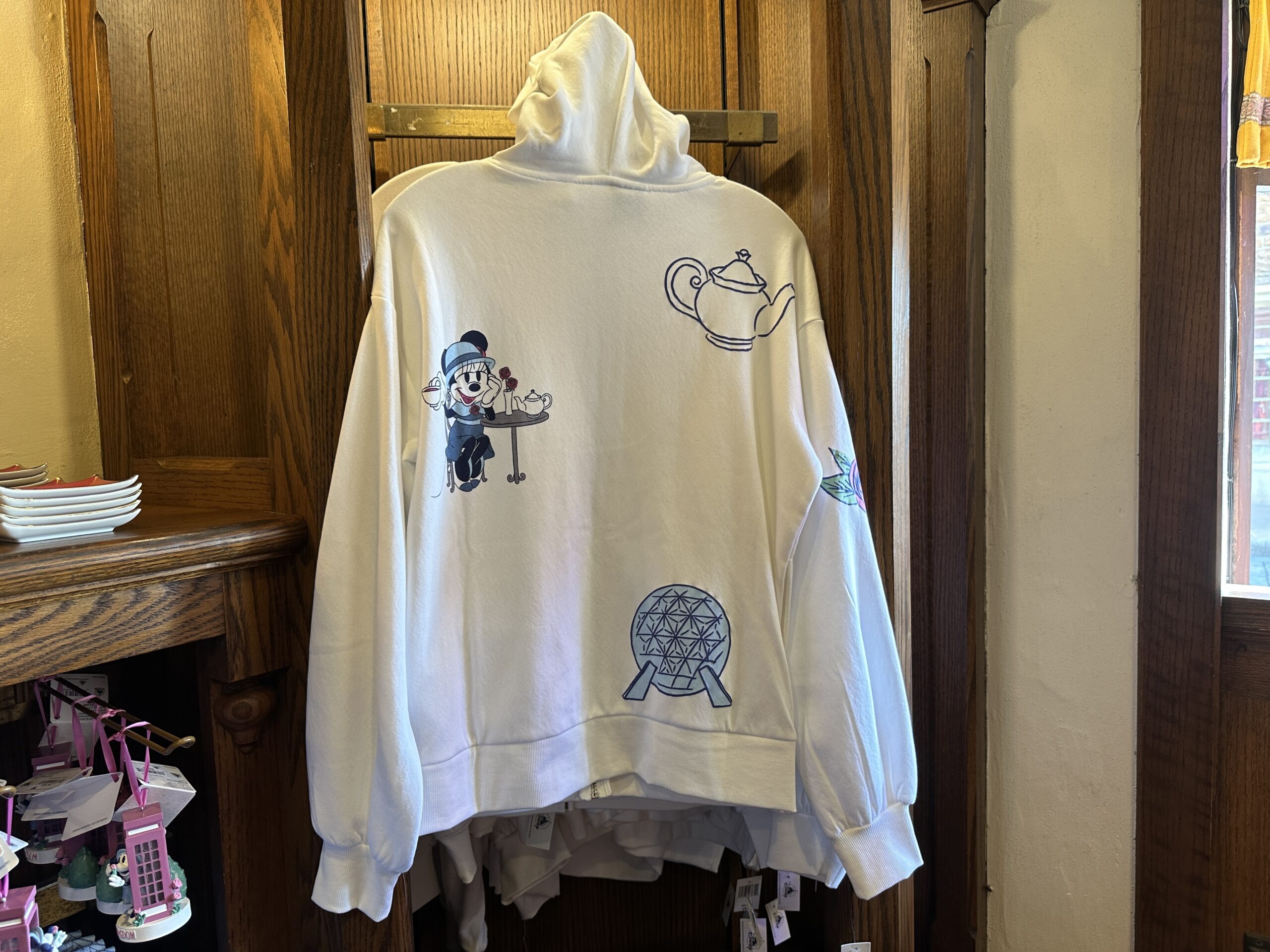 A telephone booth is pictured on the left sleeve and a rose is on the right. On the back is Minnie having tea at a table, a large tea pot, and Spaceship Earth.