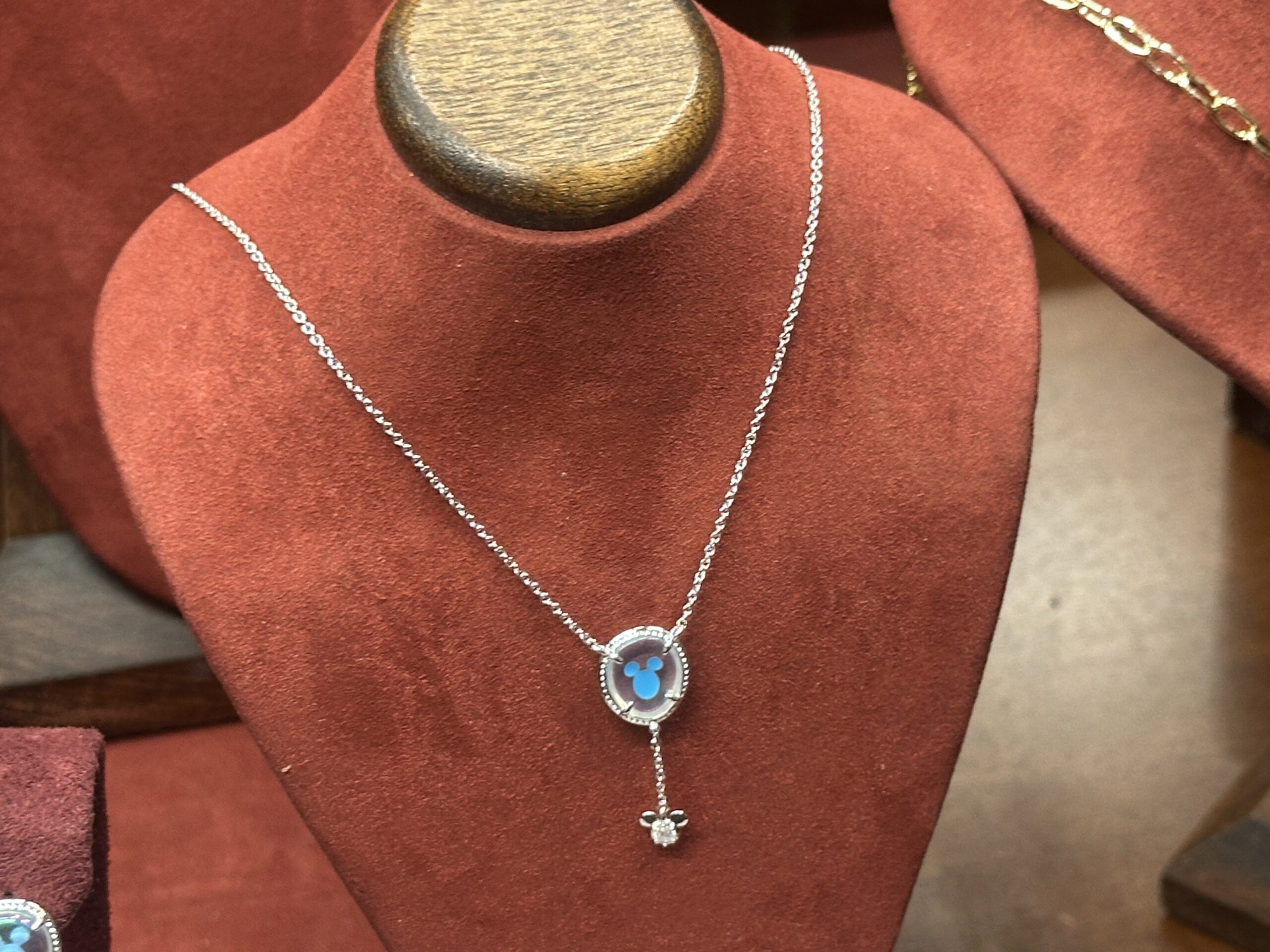 In the style of a Mickey ear balloon, this necklace by Kendra Scott shows a blue Mickey icon in the center. A dangle charm of a cubic zirconia with a pair of Mickey ears on top of it hangs down below, like the ribbon of a balloon.
