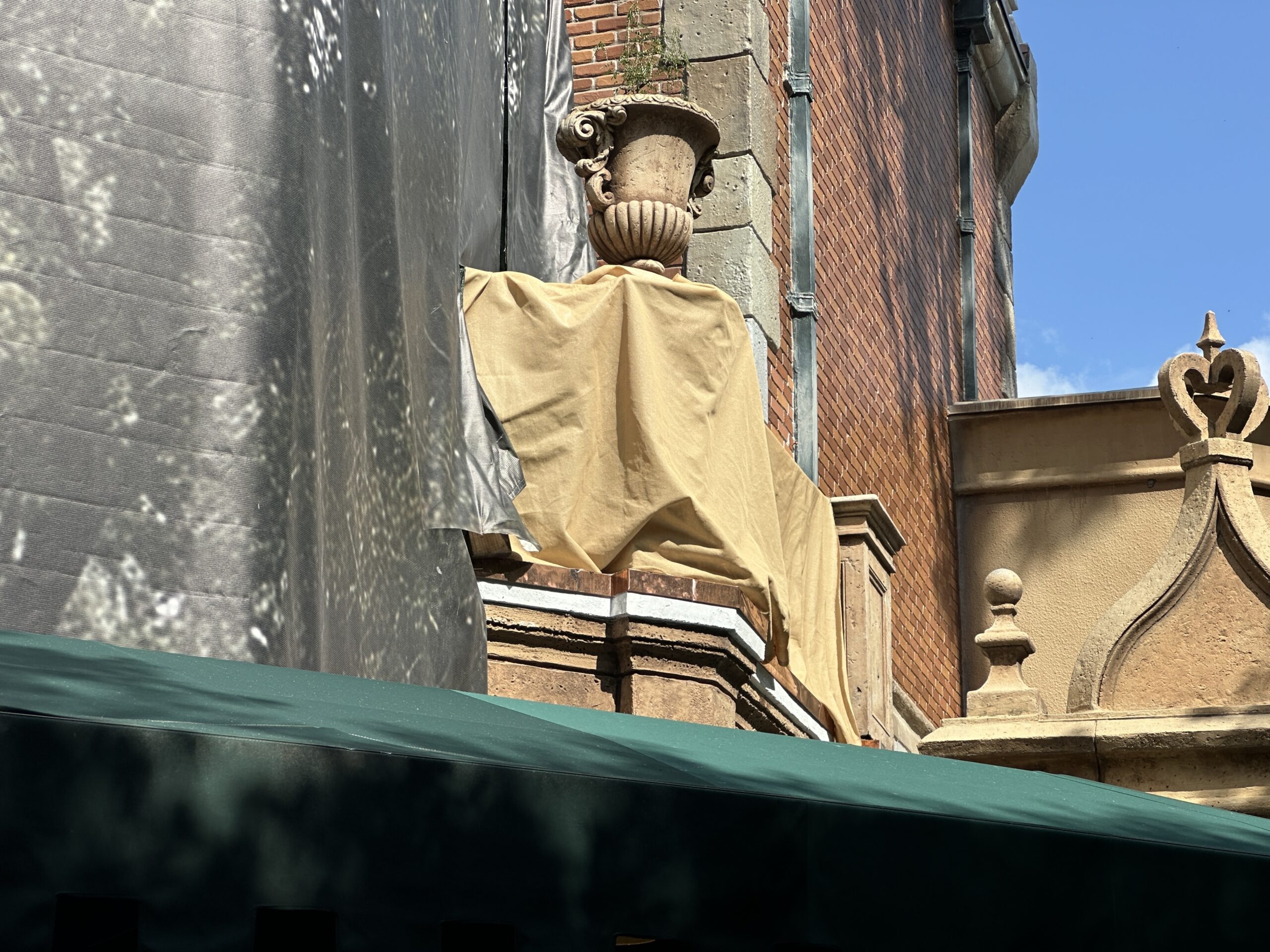 Scrims and scaffolding went up around the chimneys in March. Though scaffolding came down from one pair of chimneys in June, it went back up soon after. The scaffolding is now gone again, and it looks like the chimneys have darker detail paint, making them look more realistically burnt and soot-covered.