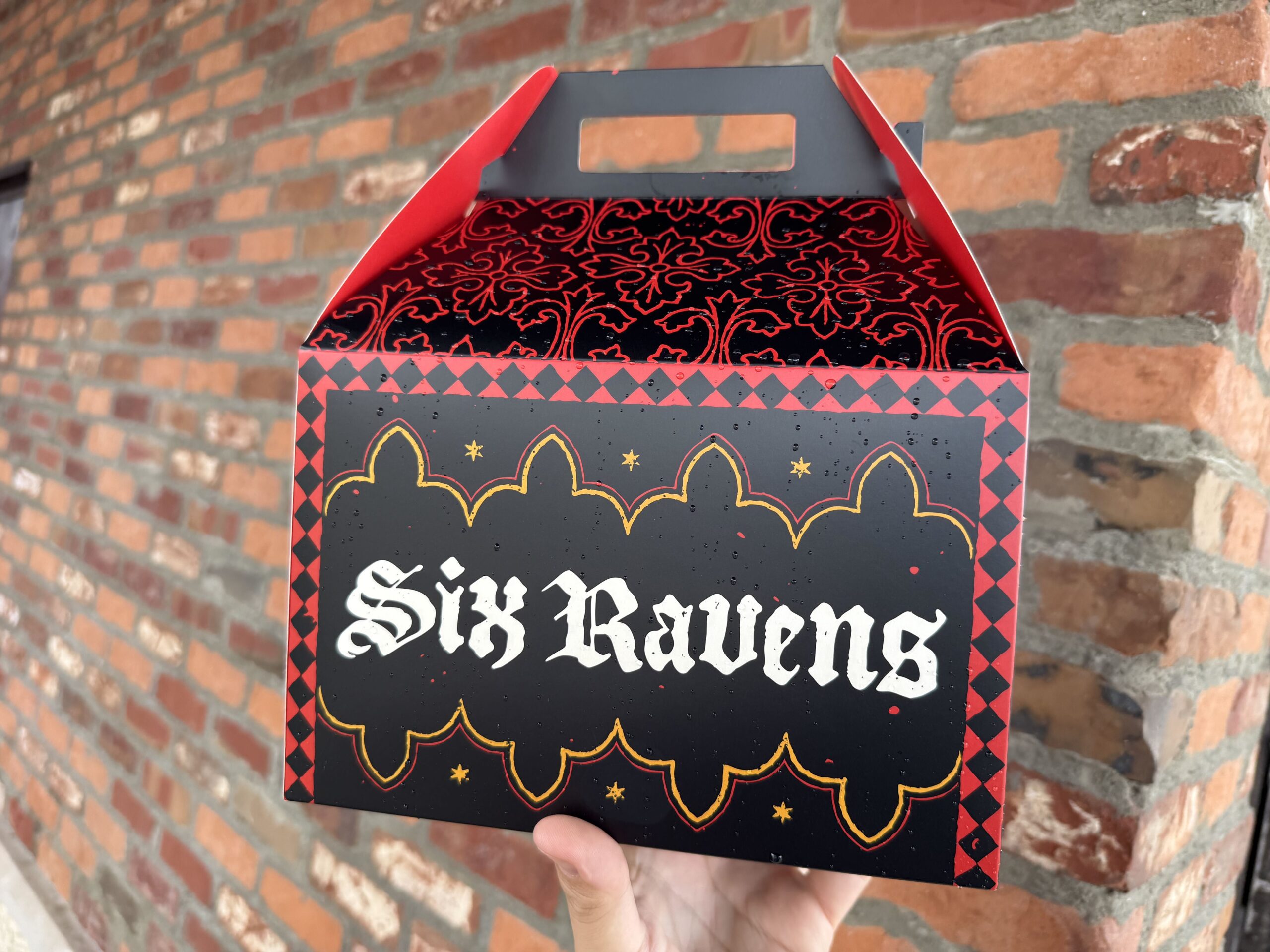 On one side is "Six Ravens" against a black background. On the reverse is the king from the restaurant's background story with "If it is good, 'tis better in a coffyn." That side opens up to create a kind of plate for eating on, featuring skeletal figures guarding a door and the six ravens with a cloaked figure.
