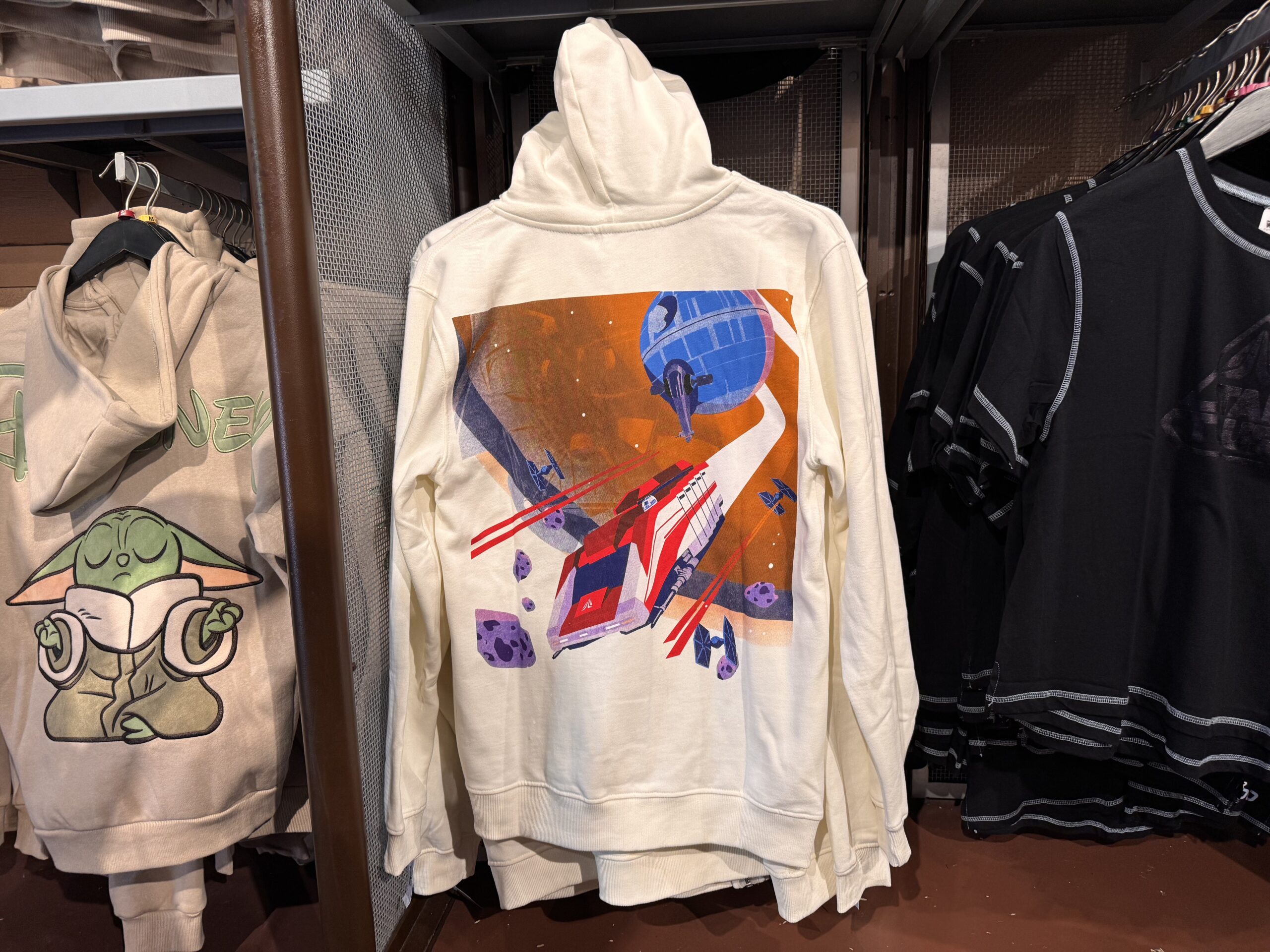 The Star Tours logo is embroidered on the front of this white hoodie. On the back is vibrant art of the StarSpeeder 1000 flying away from the Death Star among TIE Fighters.