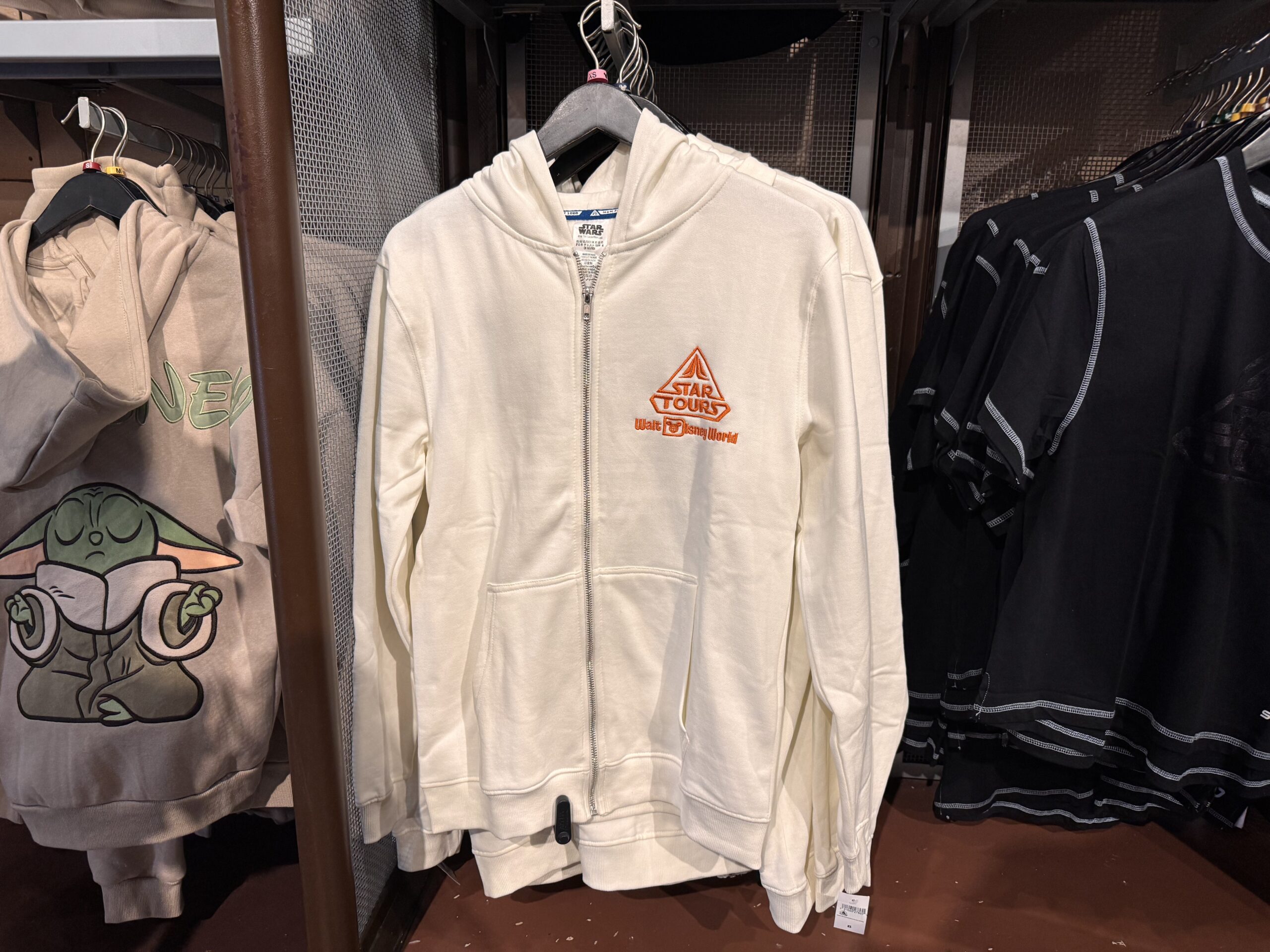 The Star Tours logo is embroidered on the front of this white hoodie. On the back is vibrant art of the StarSpeeder 1000 flying away from the Death Star among TIE Fighters.