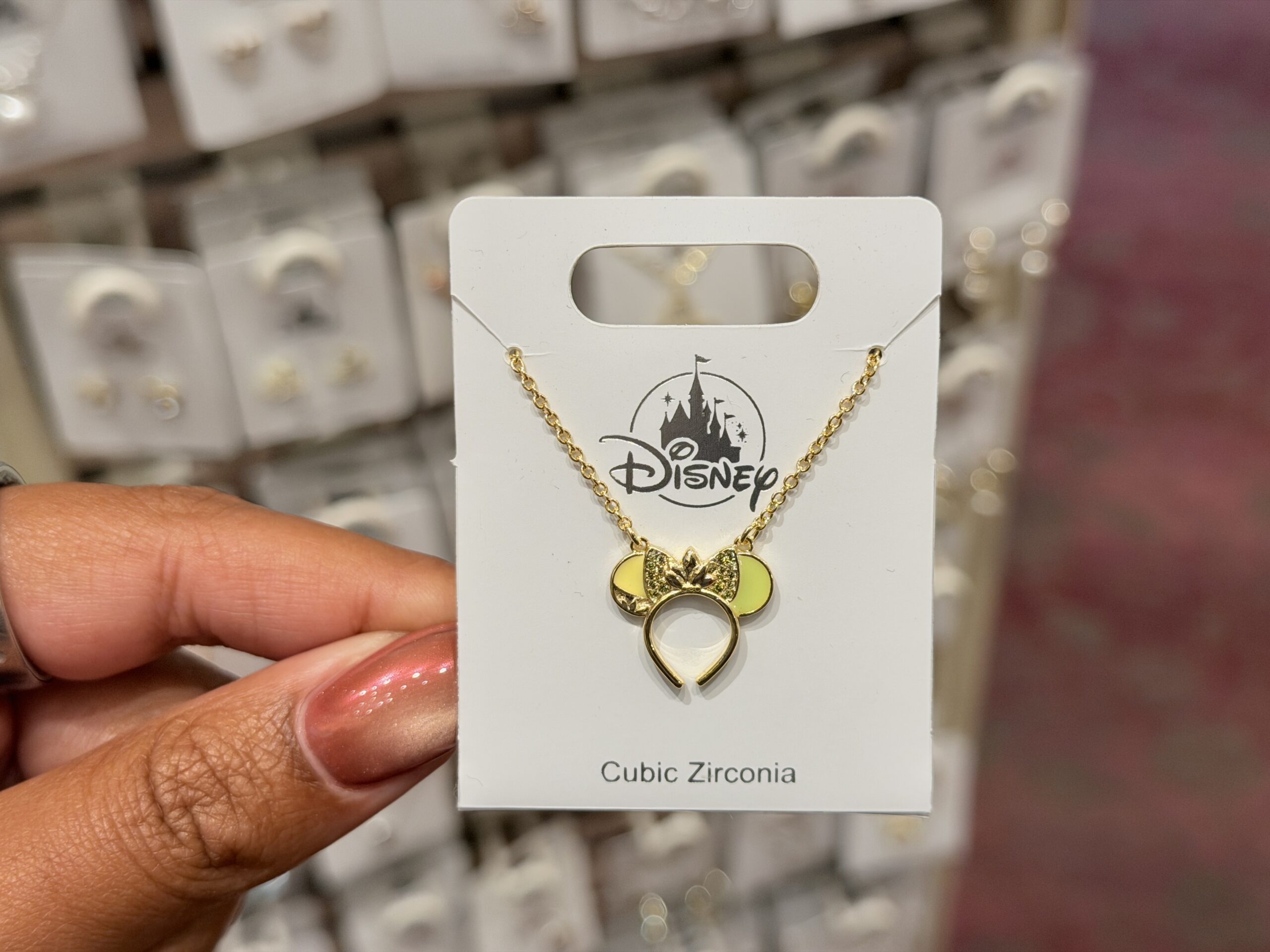 This golden necklace is inspired by Princess Tiana with a lilypad in the center of the sparkly bow. The ears are green and yellow, reminiscent of her wedding dress.