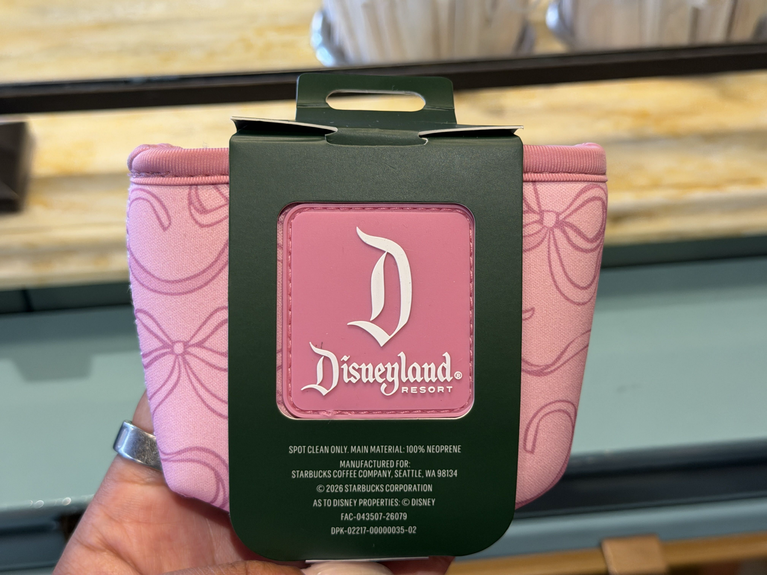 The soft pink neoprene cup sleeve features an allover bow and polka-dot design with the green Starbucks Siren logo. It is designed to fit standard Starbucks cold cups and provides a comfortable grip.