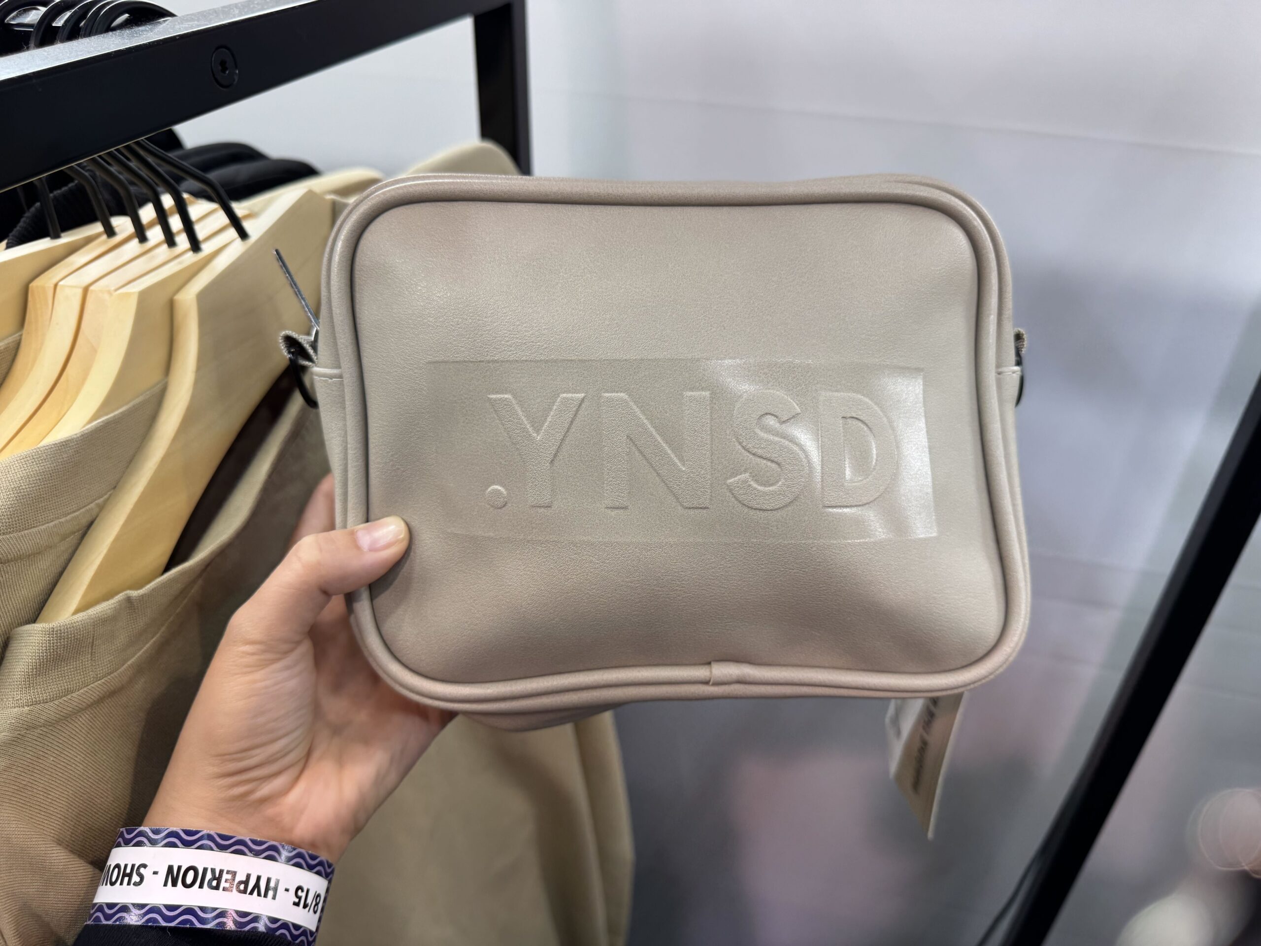 There are two crossbody bags with the .YNSD logo on the front, as well as a repeating pattern on the strap. "Imagine the Rest" is printed inside. This one is cappuccino-colored.