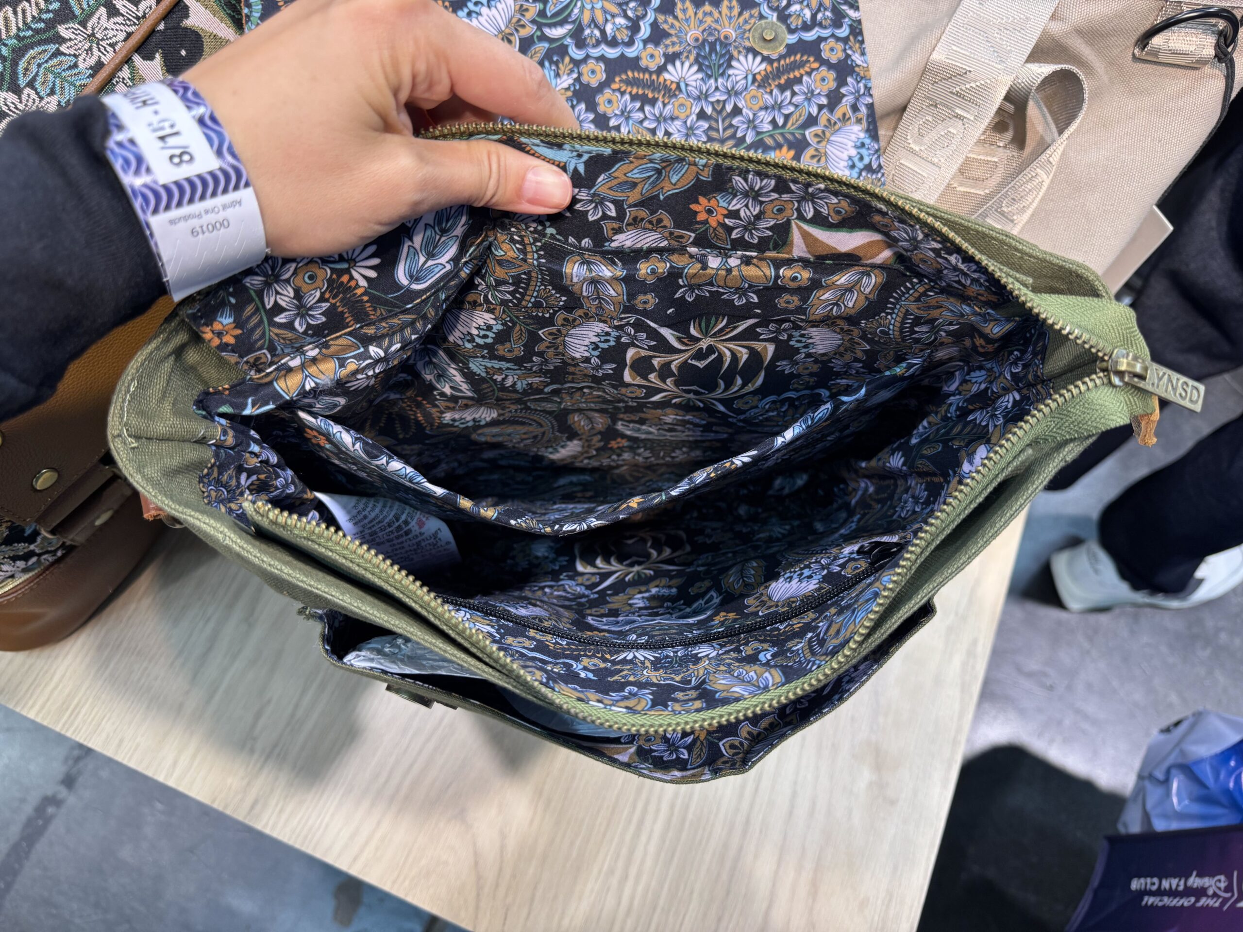 A convertible backpack is olive green and brown on one side (with the logo and Haunted Mansion spider) and carpet print on the other.