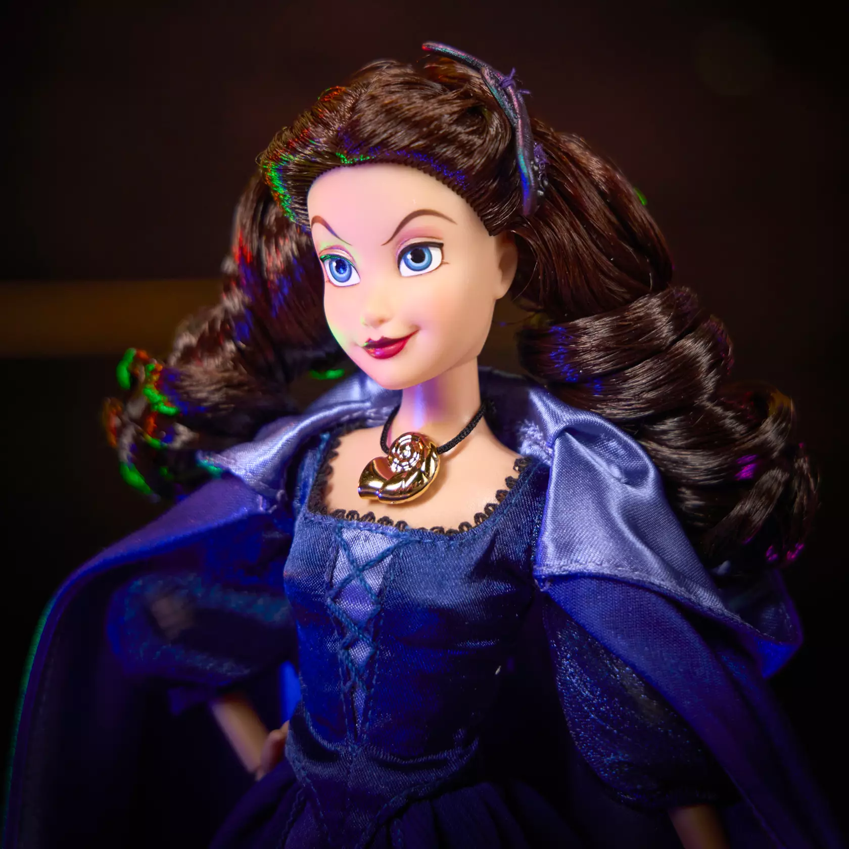 Disney Store's Autumn Special Edition 2026 doll is Vanessa, Ursula's alter ego. The 11 1/2" doll wears a purple satin gown and cape with picot trim at the neck, sheer organza puffed sleeves, and embroidered accents. Metallic foil filigree is printed on the skirt. She wears her golden nautilus shell necklace. It comes in window display packaging.