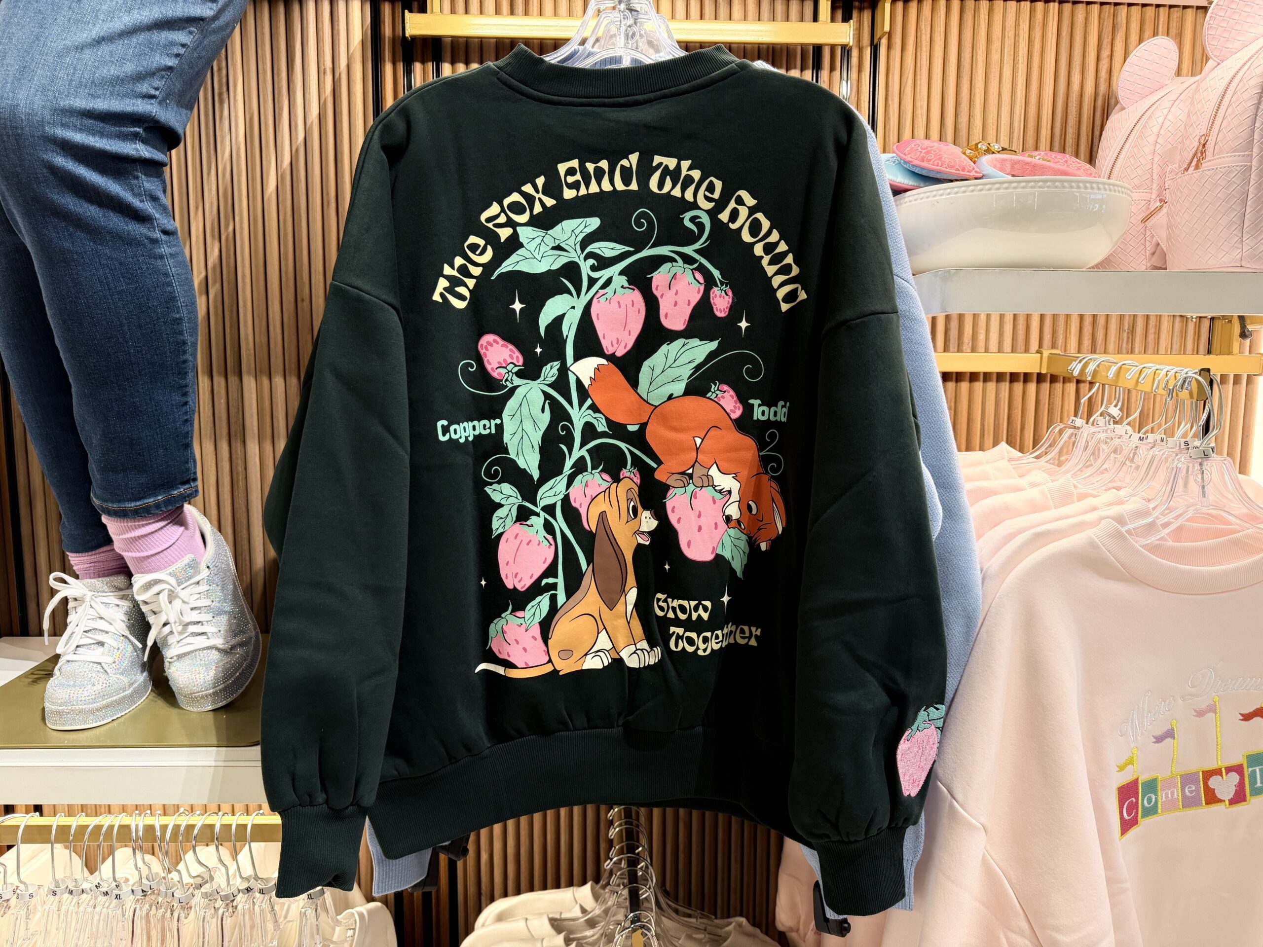 The back of the sweatshirt features a large design of Tod and Copper amongst a strawberry plant. They are both admiring the same strawberry, and the text "Grow Together" is printed beneath them.