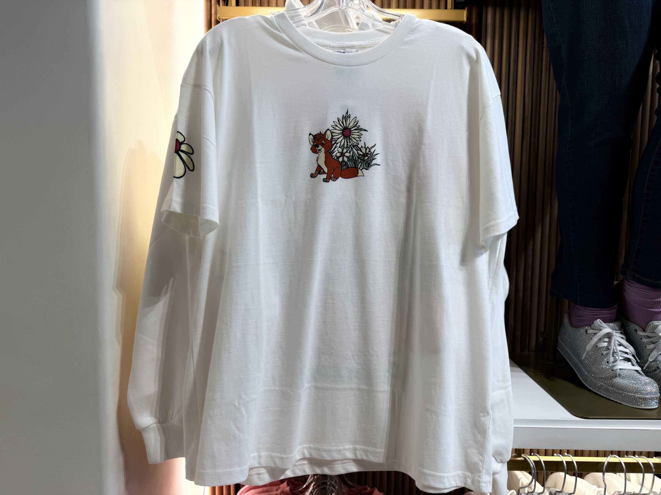 This white t-shirt has a small design on the front of Tod the fox sitting in front of white daisies. Another white daisy is embroidered on one of the short sleeves.